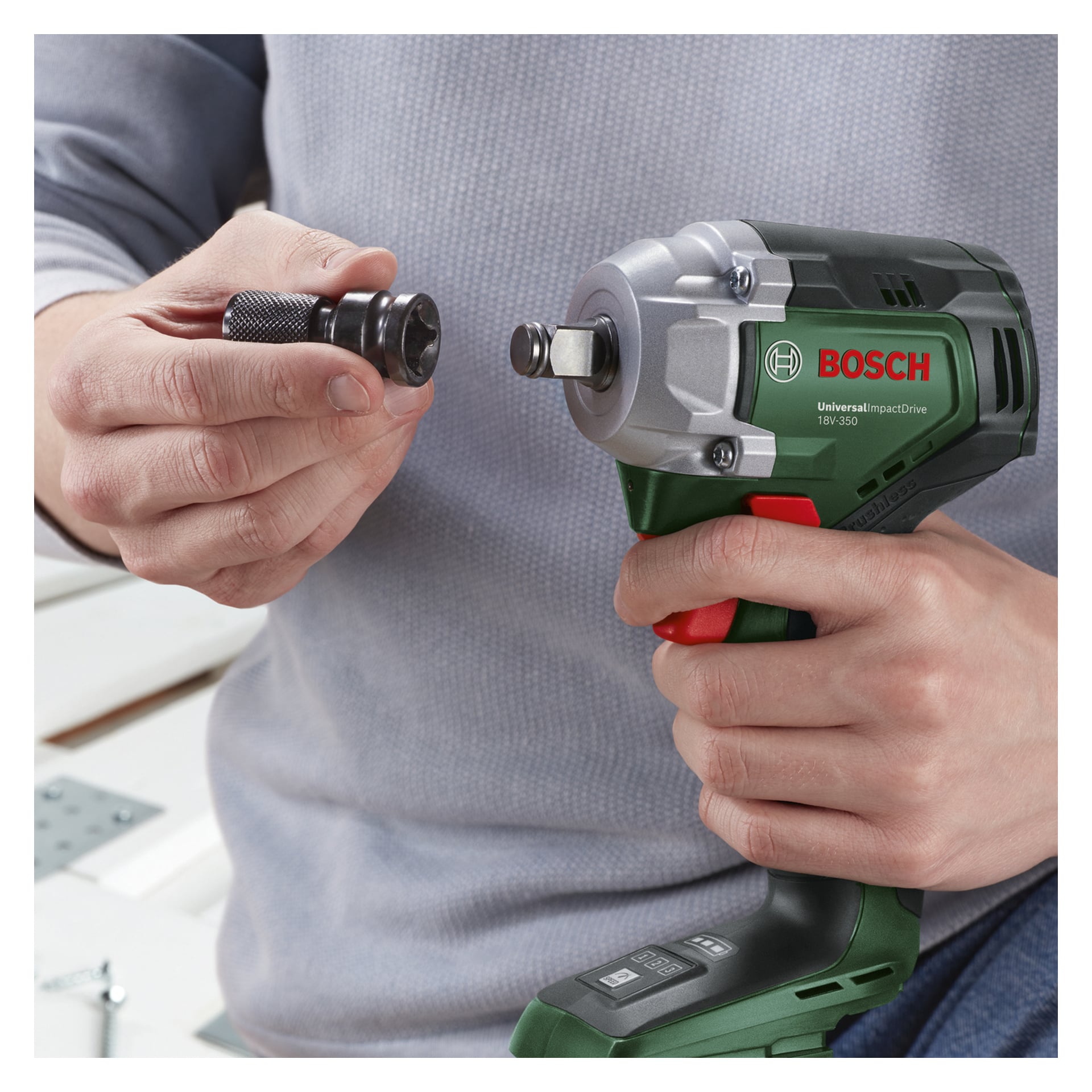 Ktoś trzyma w jednej ręce klucz udarowy Bosch Power 4 All, a w drugiej wiertło i zamierza go przymocować.