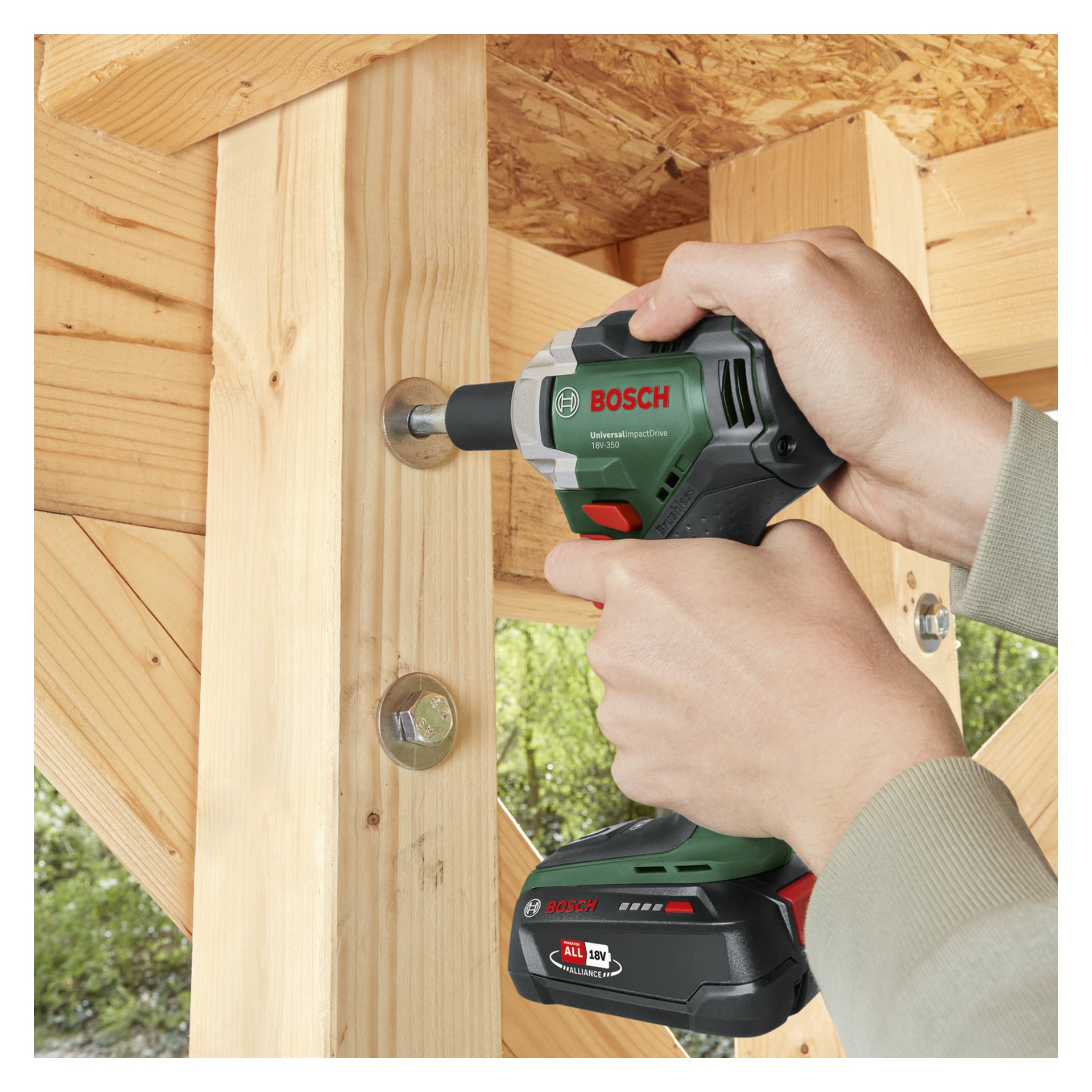 Osoba używa klucza udarowego Bosch UniversalImpactDrive 18V-350, aby dokręcić śrubę na jasnych drewnianych belkach z dużymi metalowymi mocowaniami.
