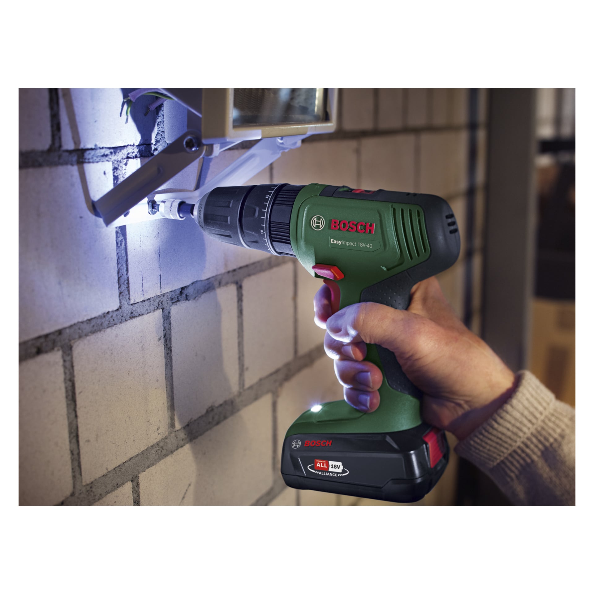 En person borrar in ett fäste i en vit tegelvägg med en Bosch Power 4 All EasyImpact 18V-40, vars inbyggda ljus lyser upp platsen.