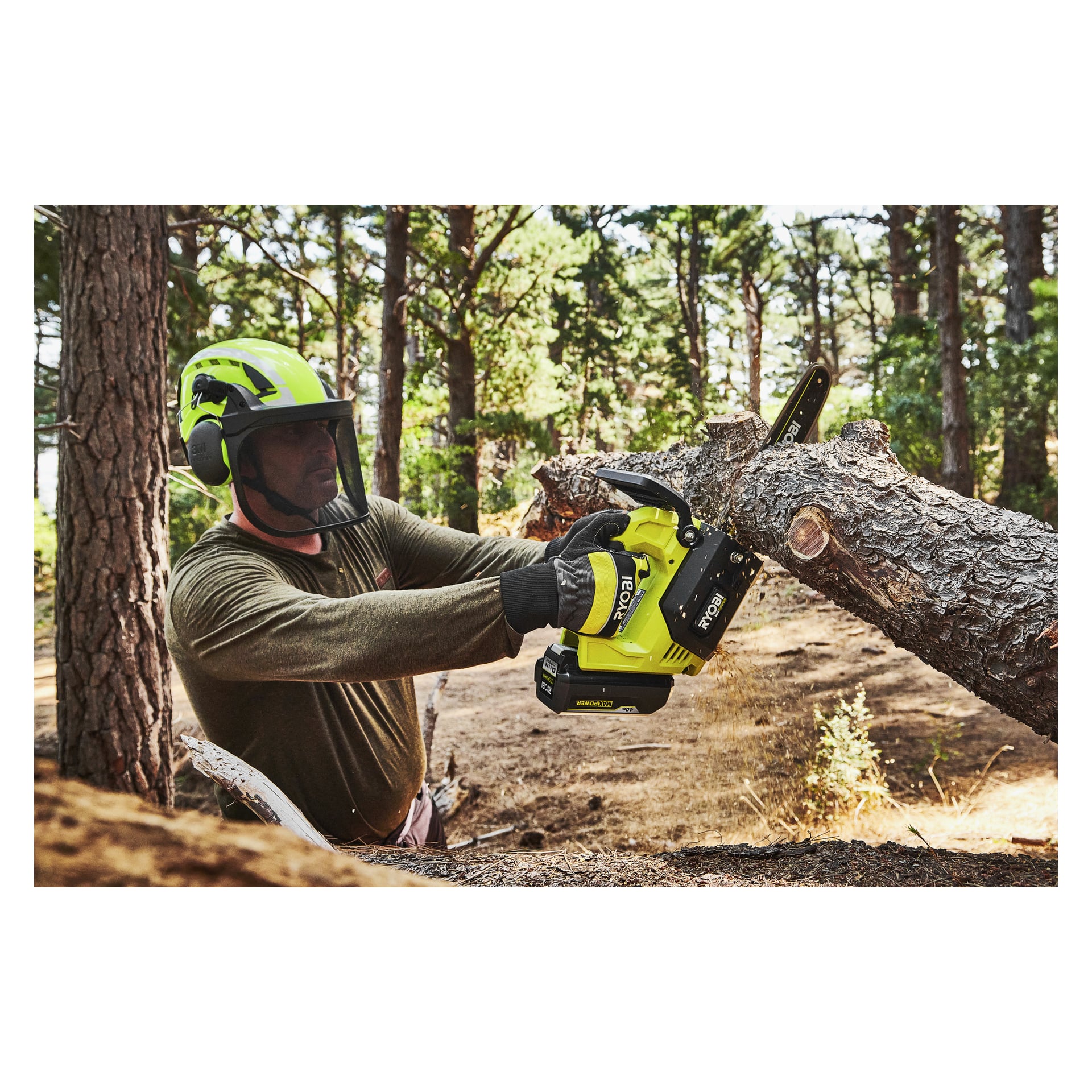En person i säkerhetsutrustning använder en grön och svart Ryobi Max Power-batterimotorsåg för att såga en tjock trädgren utomhus.