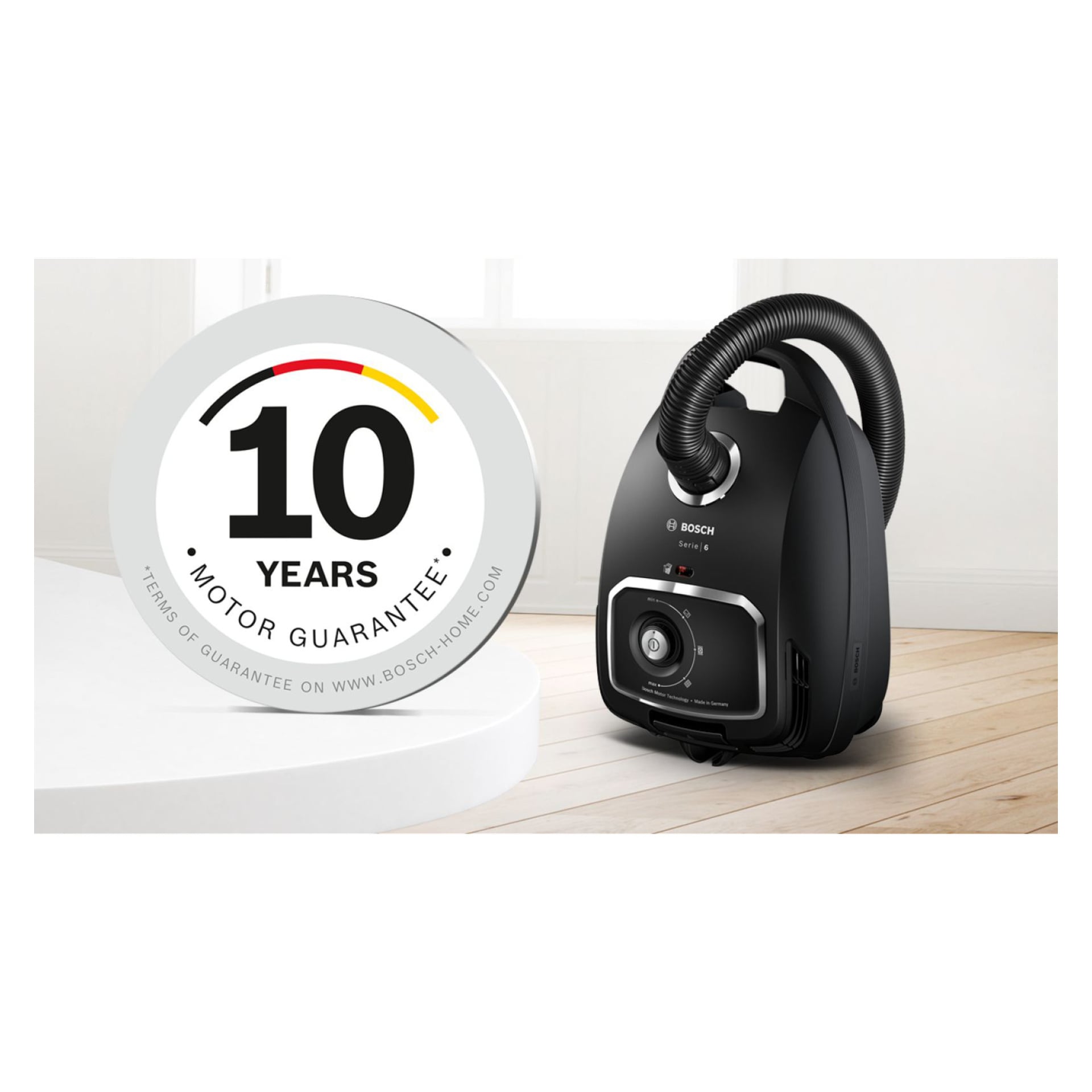 En svart Bosch Home Vacuum BGB6X320 på ett trägolv bredvid en rund bricka med texten "10 års motorgaranti" och finstilt.