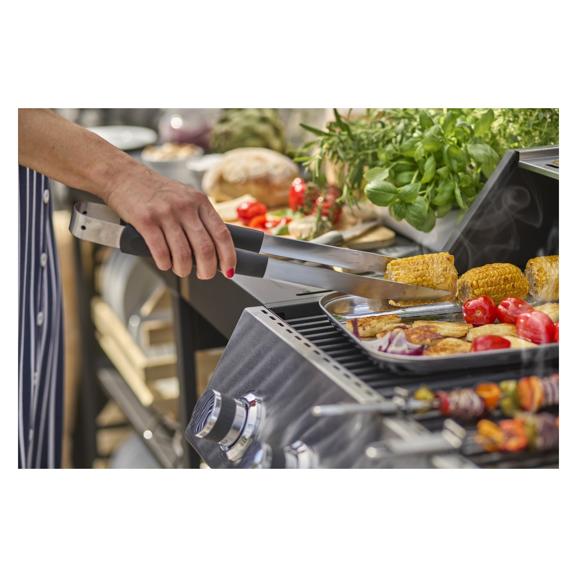 Med Burns & Barkles BBQ Tool Set grillar man majs bland tomater, lök, örter och bröd i bakgrunden.