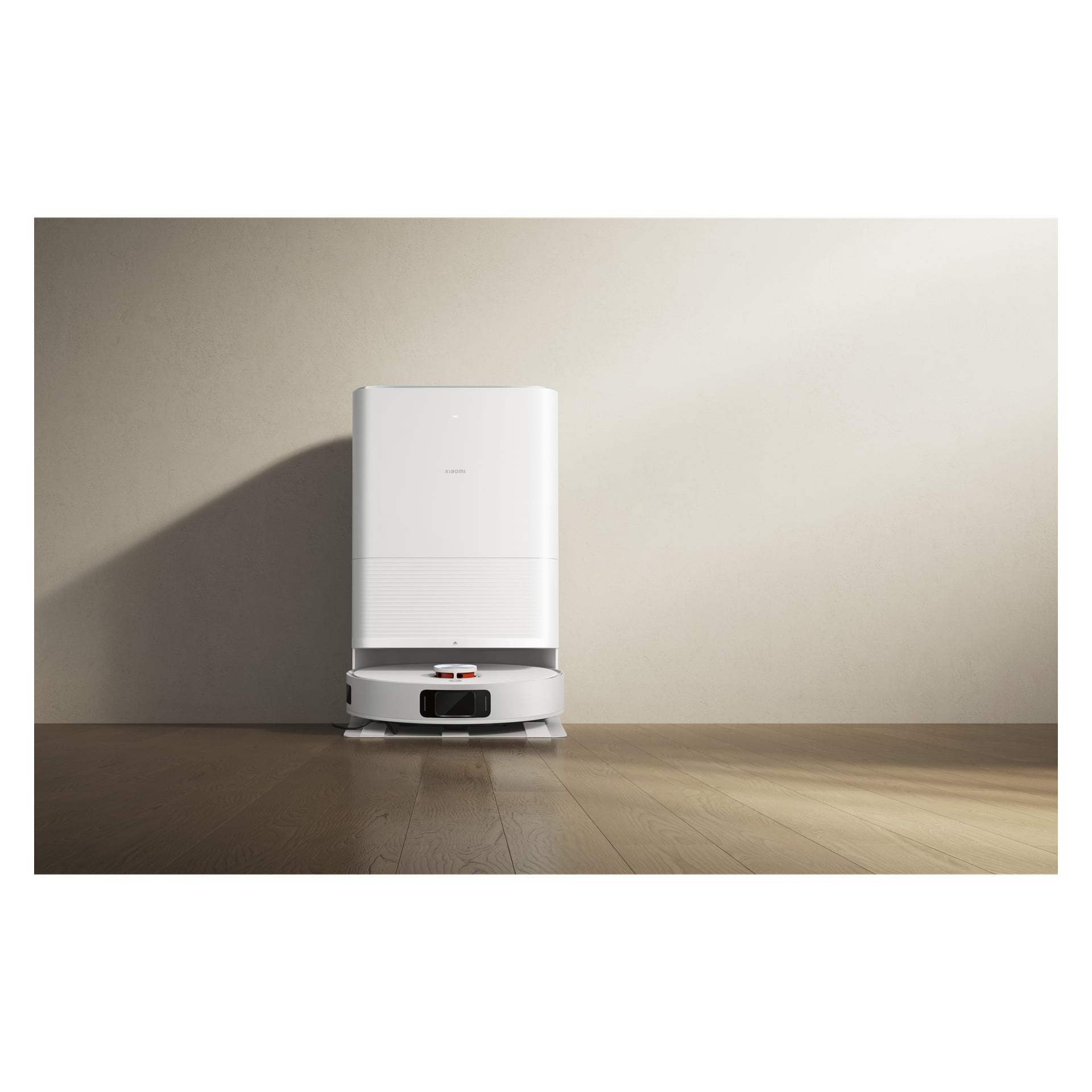 "Xiaomi Robotic Vacuum with Self-Emptying X20 Pro" oraz jego stacja dokująca spoczywają na drewnianej podłodze obok beżowej ściany, rzucając delikatne cienie.