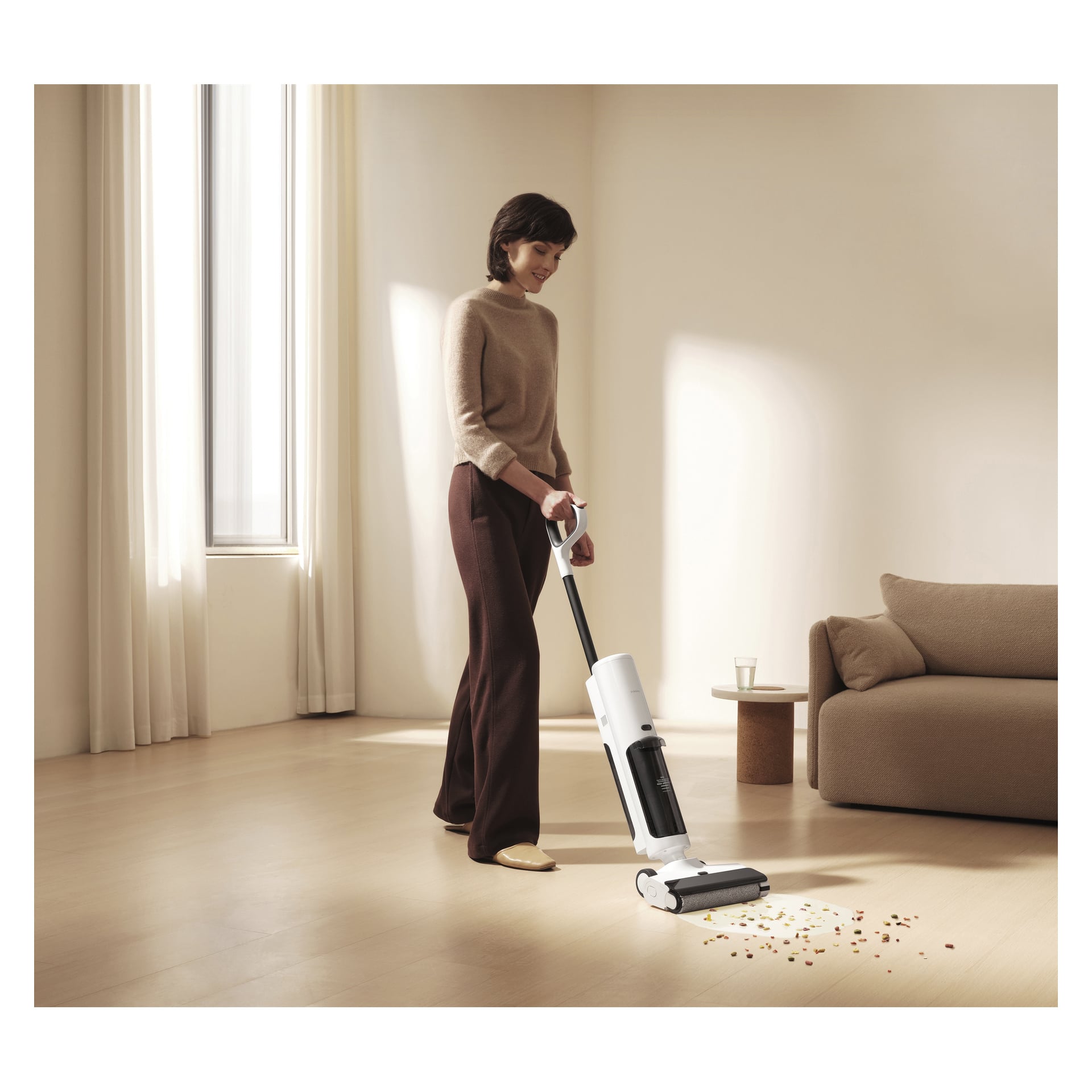 Jemand entfernt kleine Abfälle von einem hellen Holzboden mit einem Xiaomi 3-in-1-Staubsauger in einem minimalistischen Wohnzimmer mit beigefarbenen Wänden.