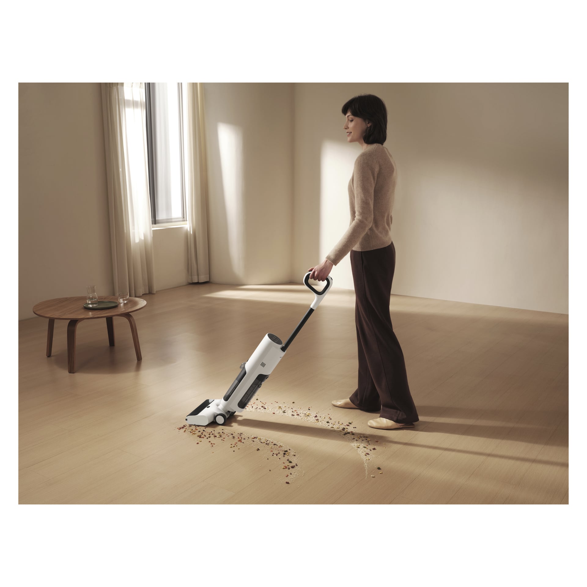 Jemand in einem beigen Pullover und dunklen Hosen saugt in einem minimalistischen Raum Ablagerungen von einem hellen Holzboden mit einem Xiaomi Truclean W20.