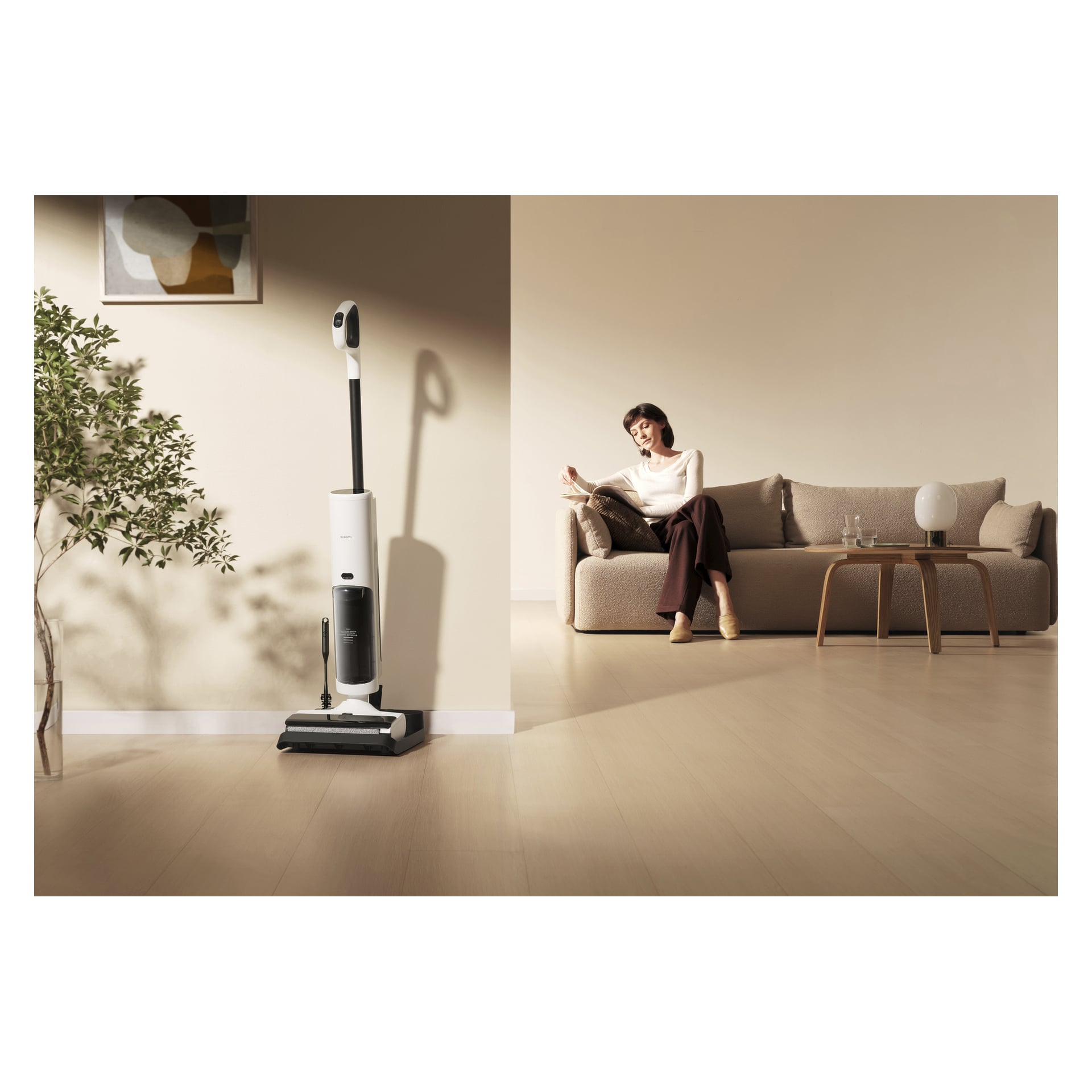 Eine Frau entspannt sich auf einem beigefarbenen Sofa in einem einfachen Wohnzimmer, während der Xiaomi Truclean W20 Staubsauger neben einer Topfpflanze und einem Tisch steht.