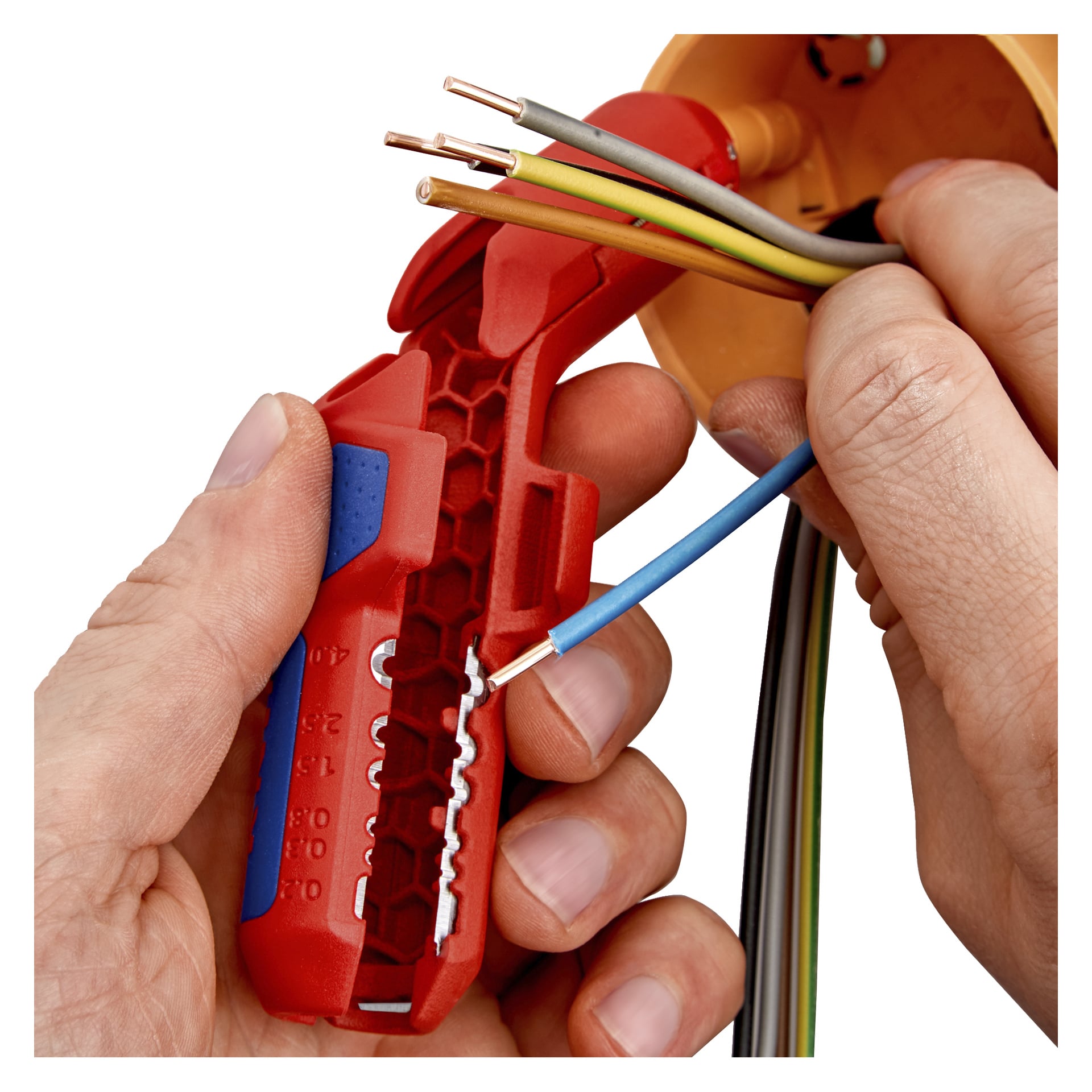 En person bruker Knipex ErgoStrip 3-i-1 kabelstripper for å fjerne isolasjon fra en blå ledning ved siden av en oransje elektrisk boks.