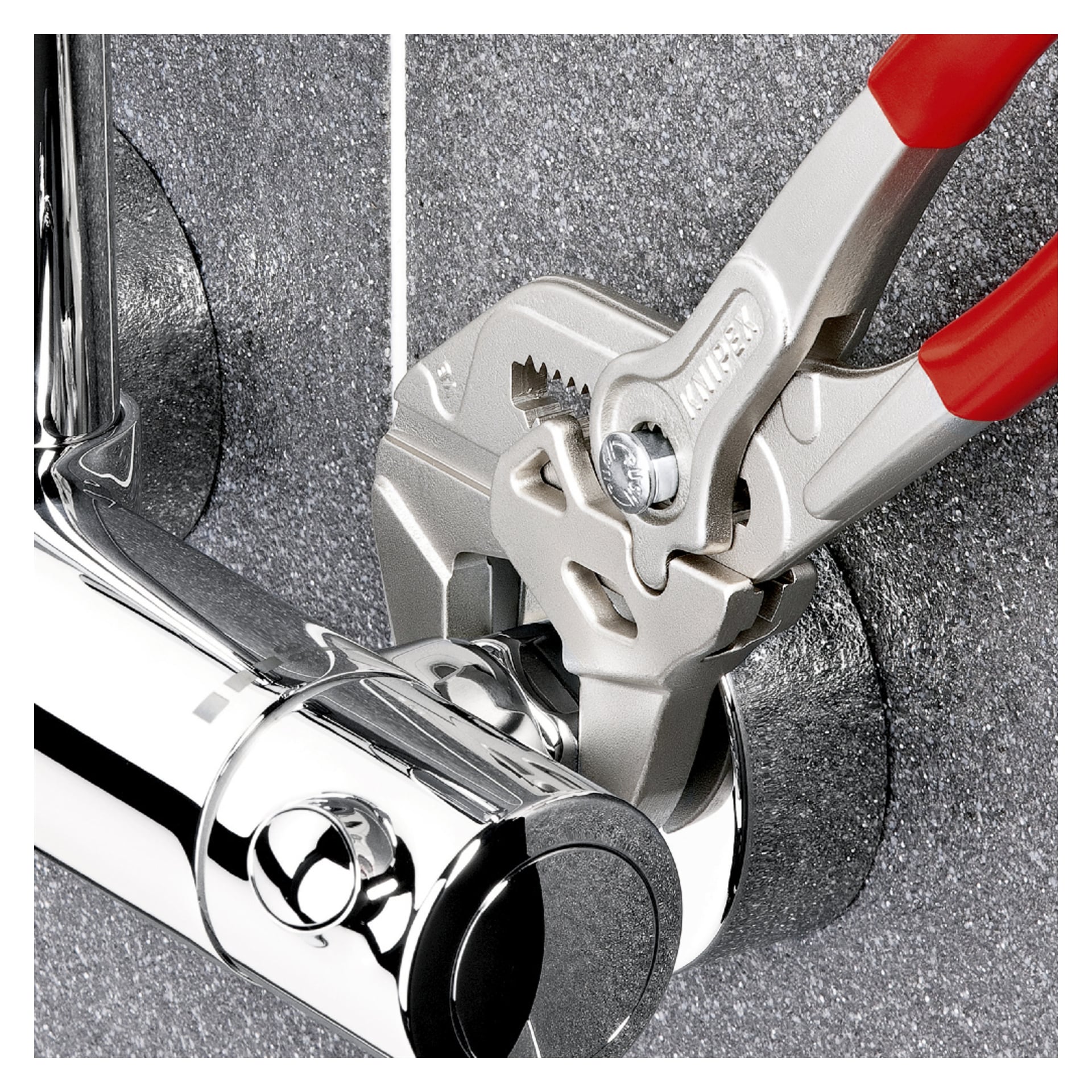En Knipex Tängnyckel 86 03 150 SB med röda handtag greppar en kromrörskoppling mot en grå texturerad vägg.