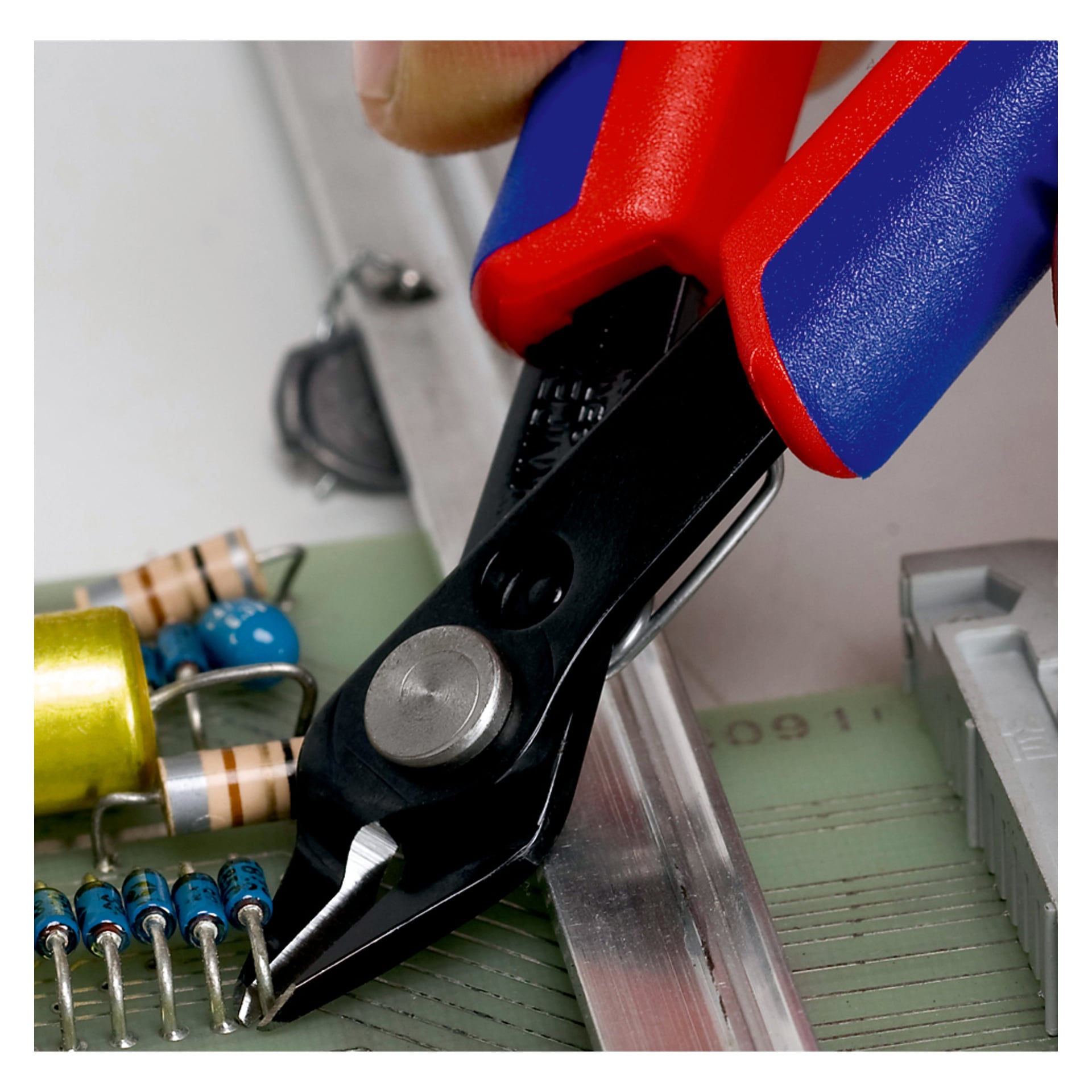 Närbild av Knipex Electronic Super Knips sidoskärtång med röda och blå handtag som trimmar ledningar nära motstånd på ett kretskort.