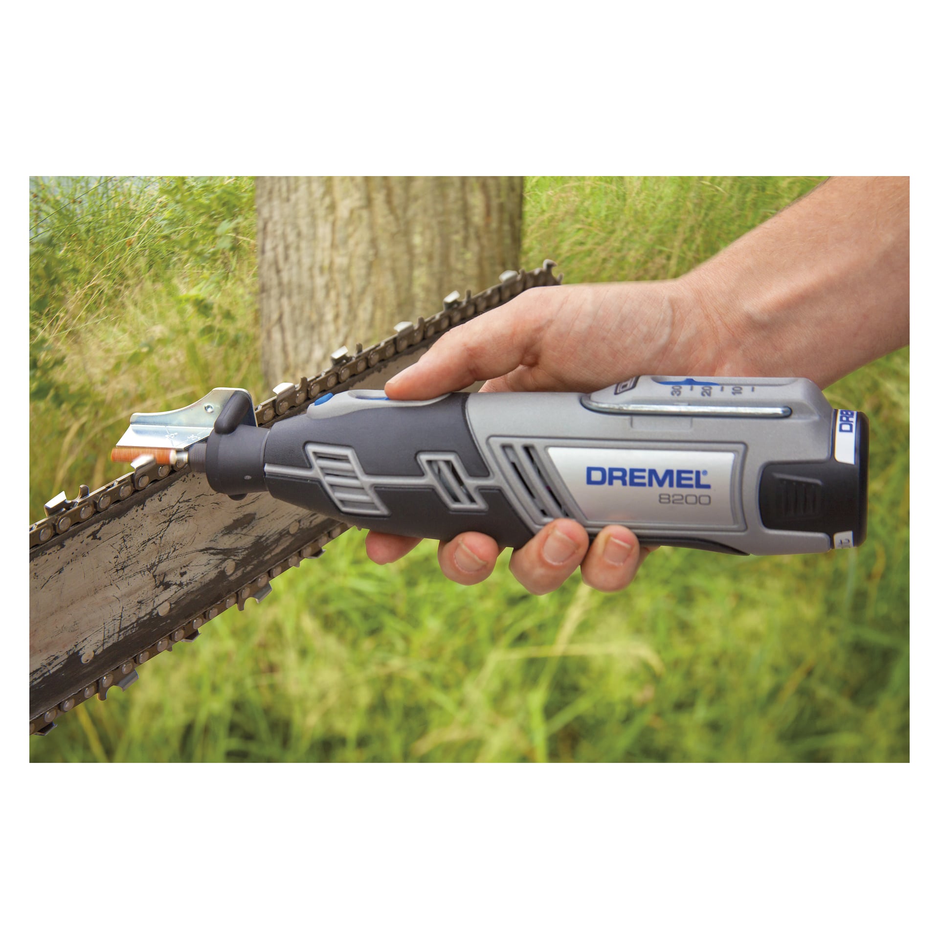 Man använder Dremel 1453 motorsågsslipningsset utomhus, med gräs och en trädstam i bakgrunden.