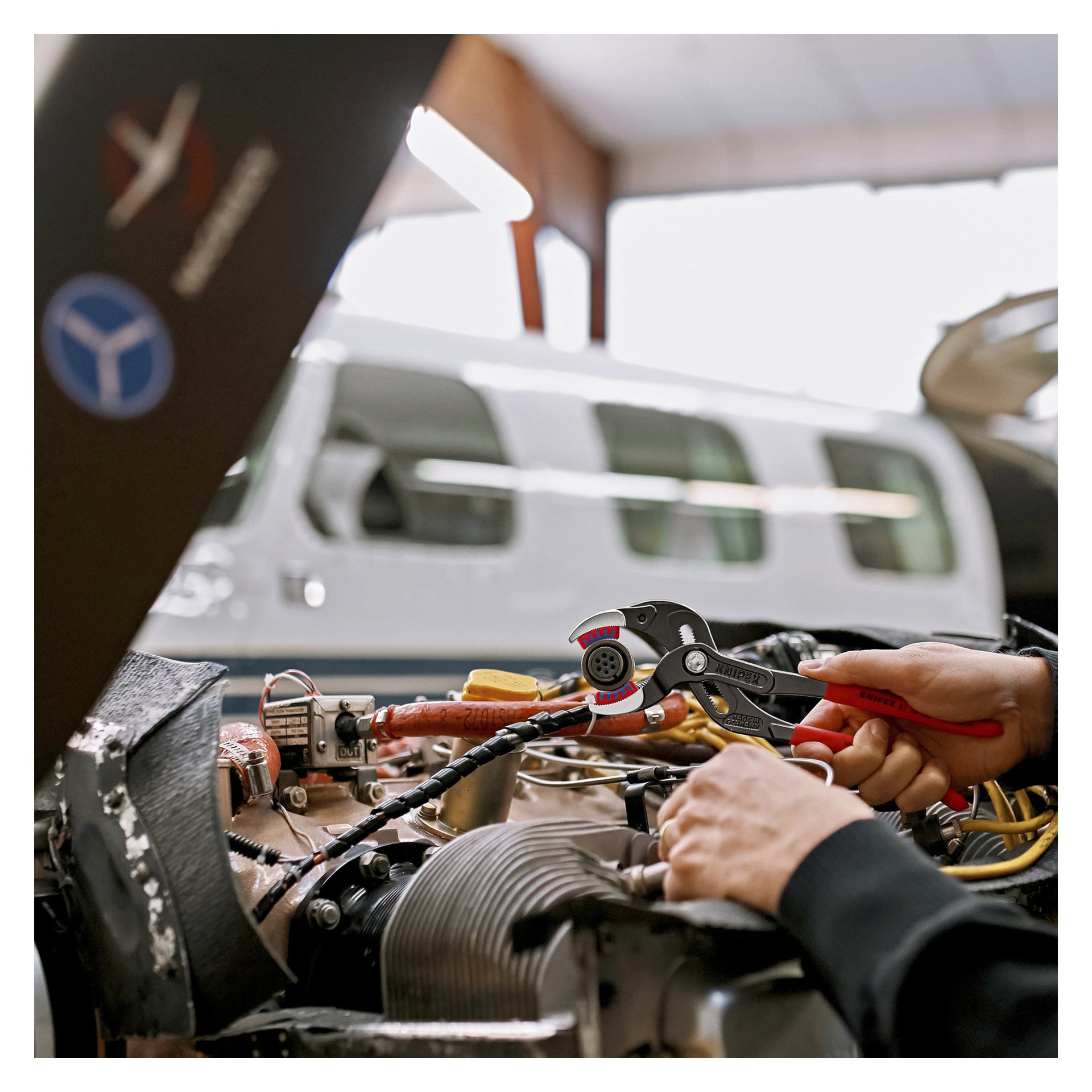 Någon justerar en flygplansmotordel med Knipex vattenpumpstång 81 11 250 SB; Ett flygplan syns bakom i en hangar.
