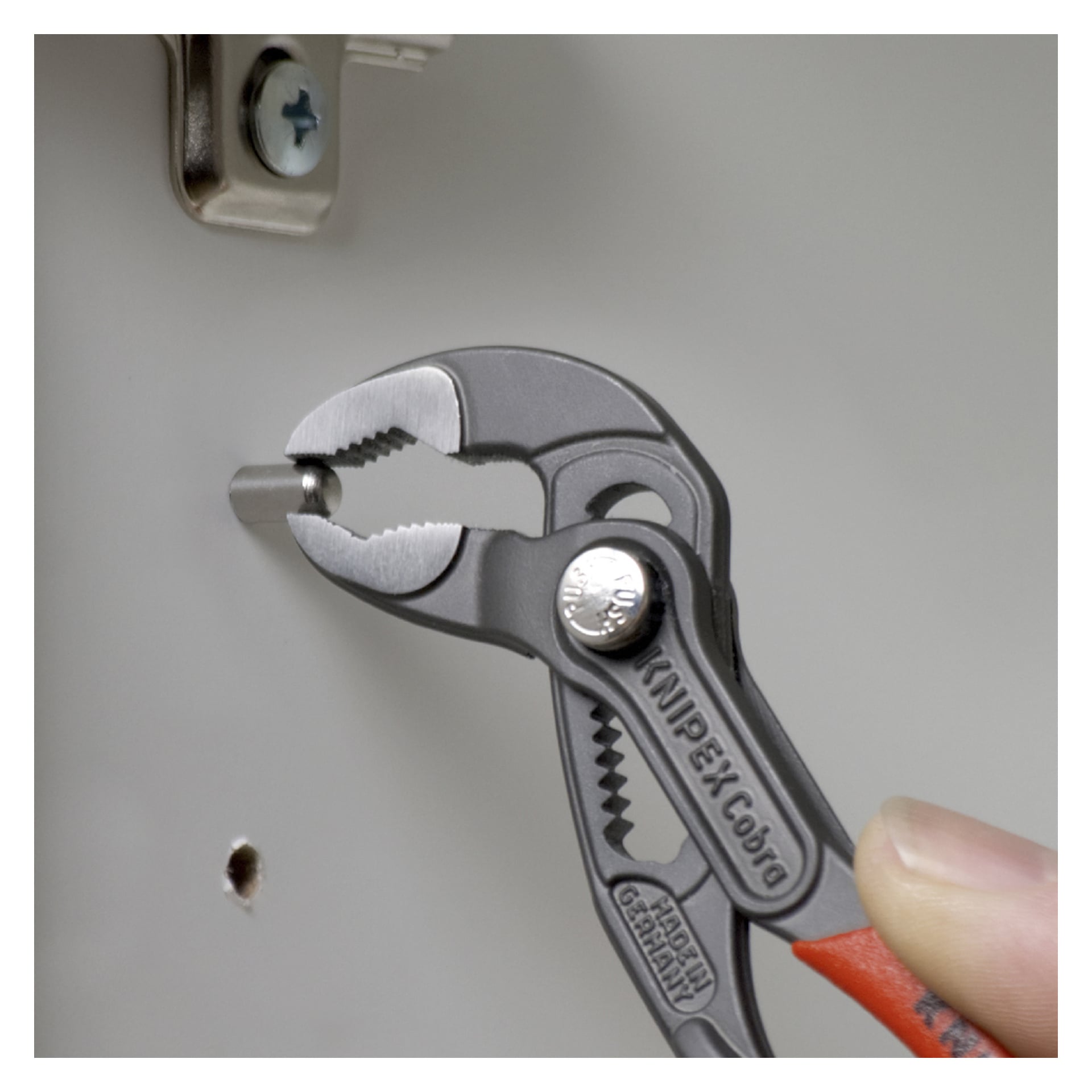 Ręka chwyta metalowy element szczypcami pompy wodnej Knipex Cobra, blisko włącznika mocowanego na śrubę i pustego otworu na śrubę.