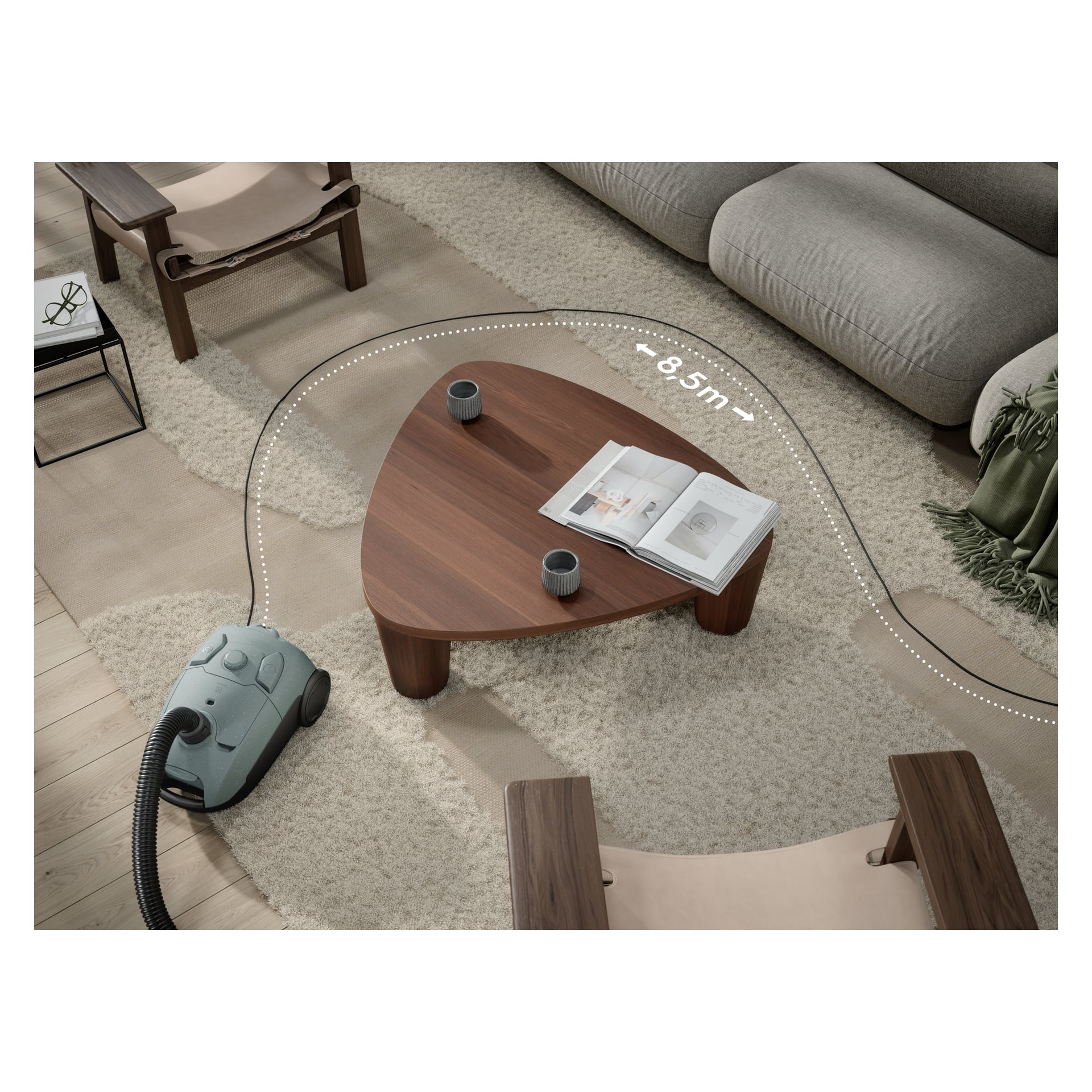 Electrolux Clean 500 EB51C1OG stoi na beżowym dywanie przy drewnianym stoliku kawowym, z przerywaną linią pokazującą jego 8,5 m zasięgu.