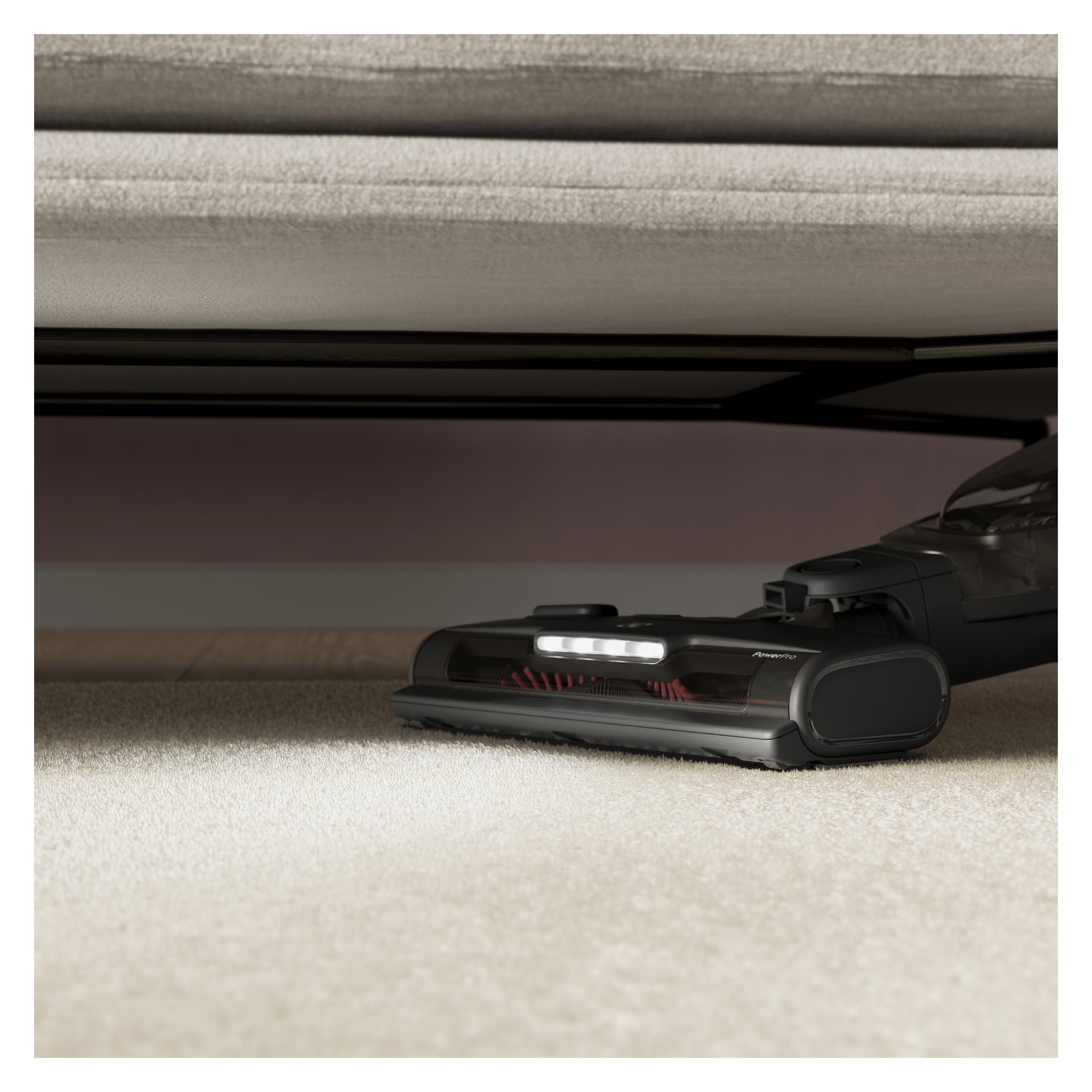 En Electrolux Upright 500 Clean støvsuger med lavprofil hode og LED-lys støvsuger teppe under en sofa.