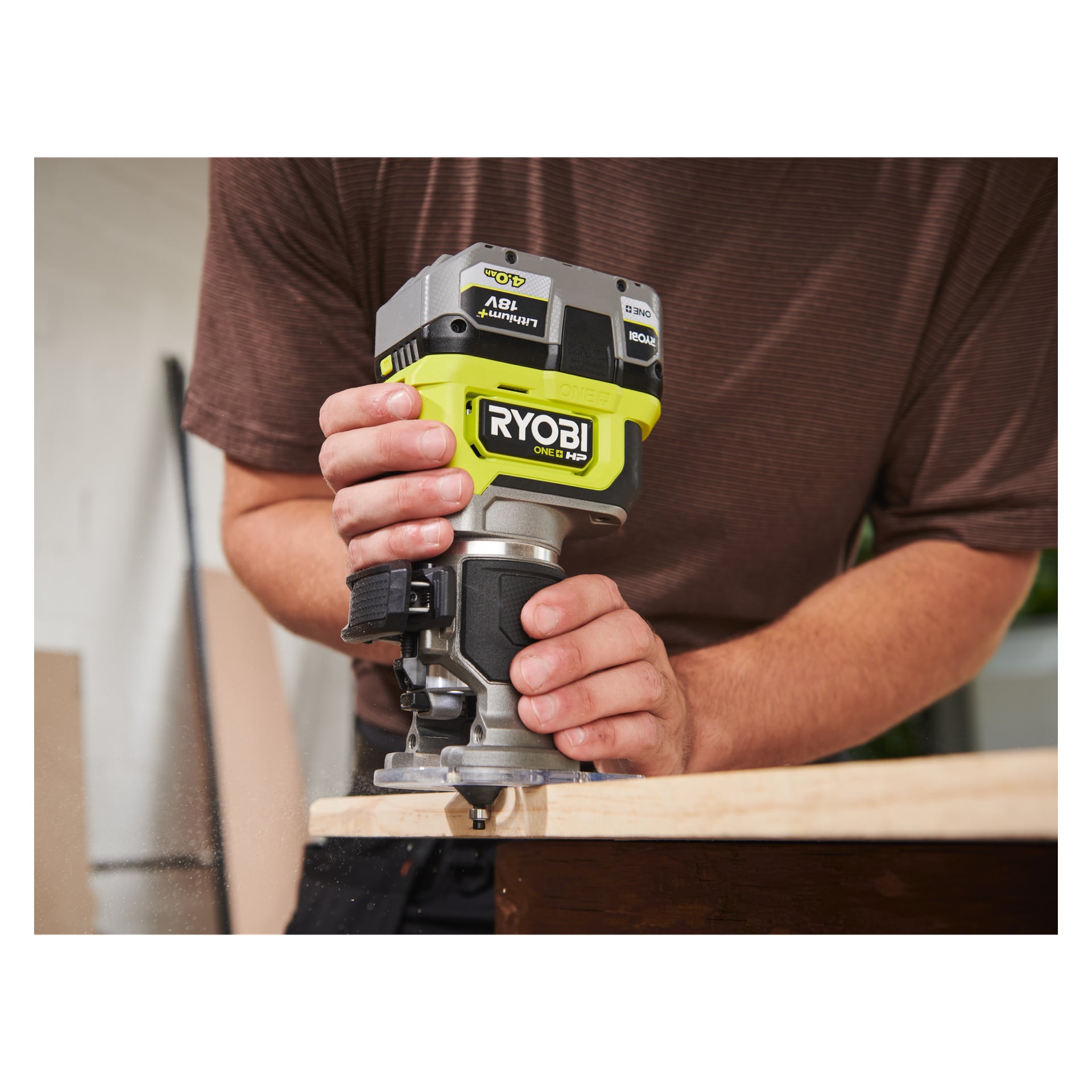 Noen bruker en Ryobi One+ HP håndholdt ruter RTR18C-0 langs kanten av en treplate, med spredte fliser under.