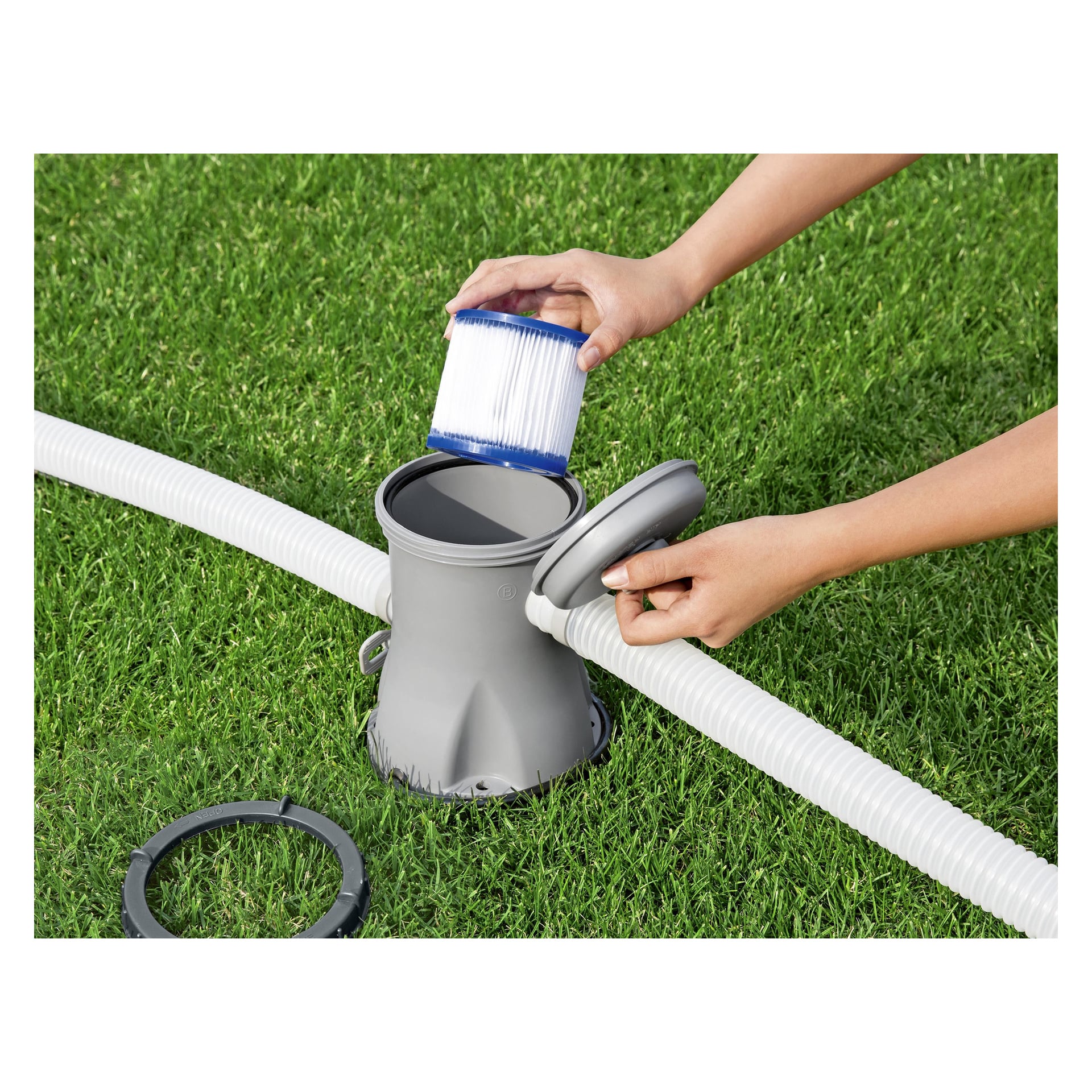 Man holder en Bestway Pool Filter Cartridge (I) 2-pack over et åpent grått bassengpumpefilter på gress, slanger og pakning synlig.