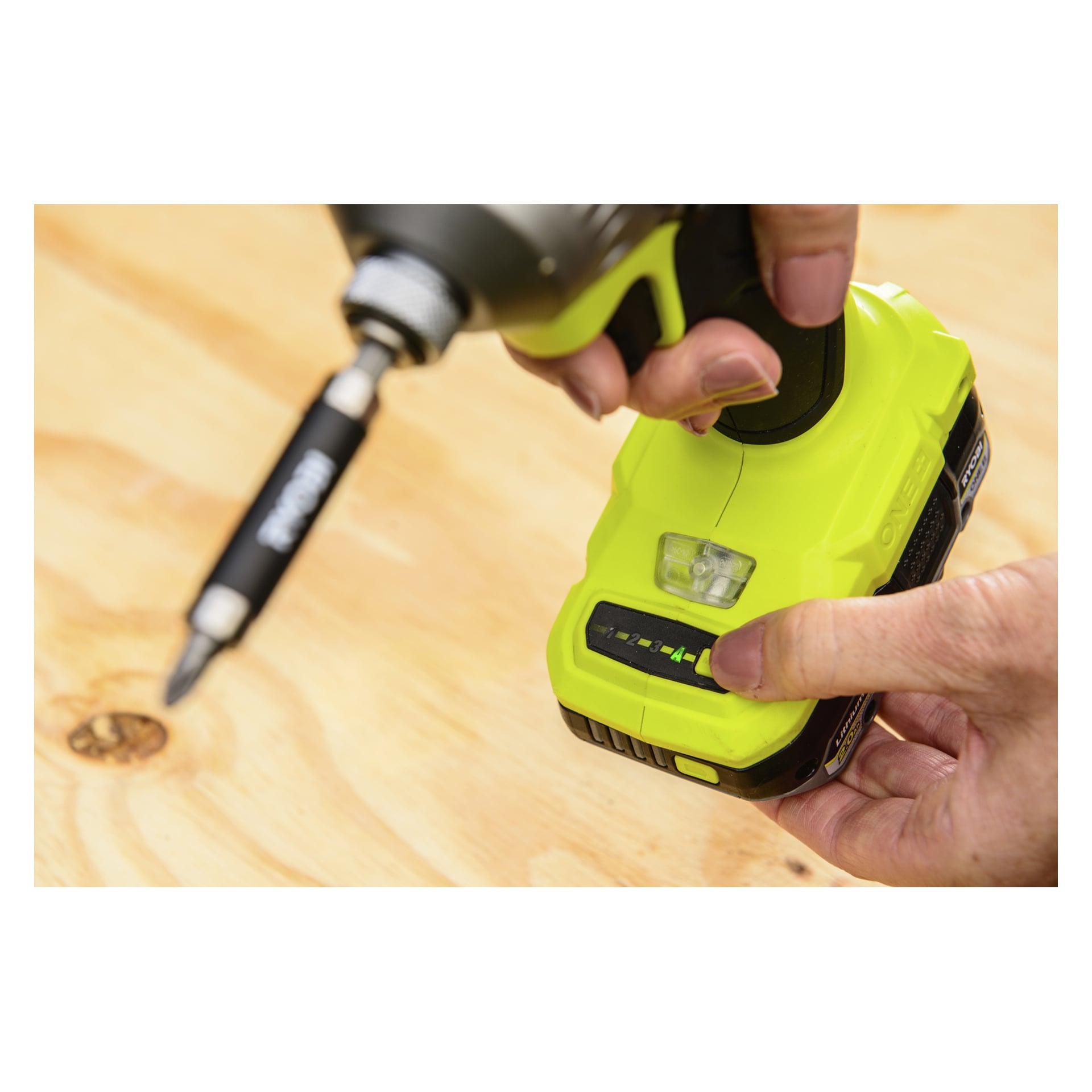 Någon kollar batterinivån på en ljusgrön Ryobi One+ HP Brushless slagdragare RID18X1-0 mot en träbakgrund.