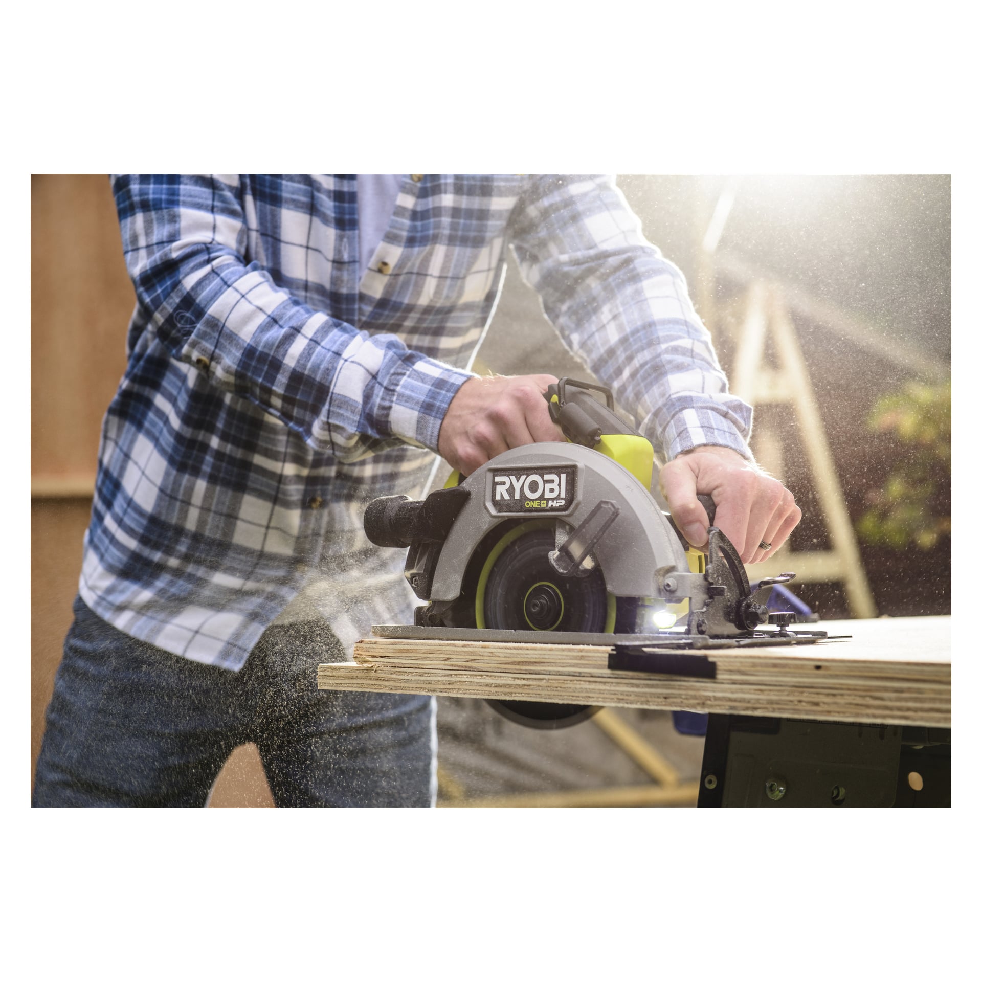 Iført en blå rutete skjorte styrer noen en Ryobi One+ HP rundsag RCS18X1-0 på tre mens sagflis sprer seg rundt.