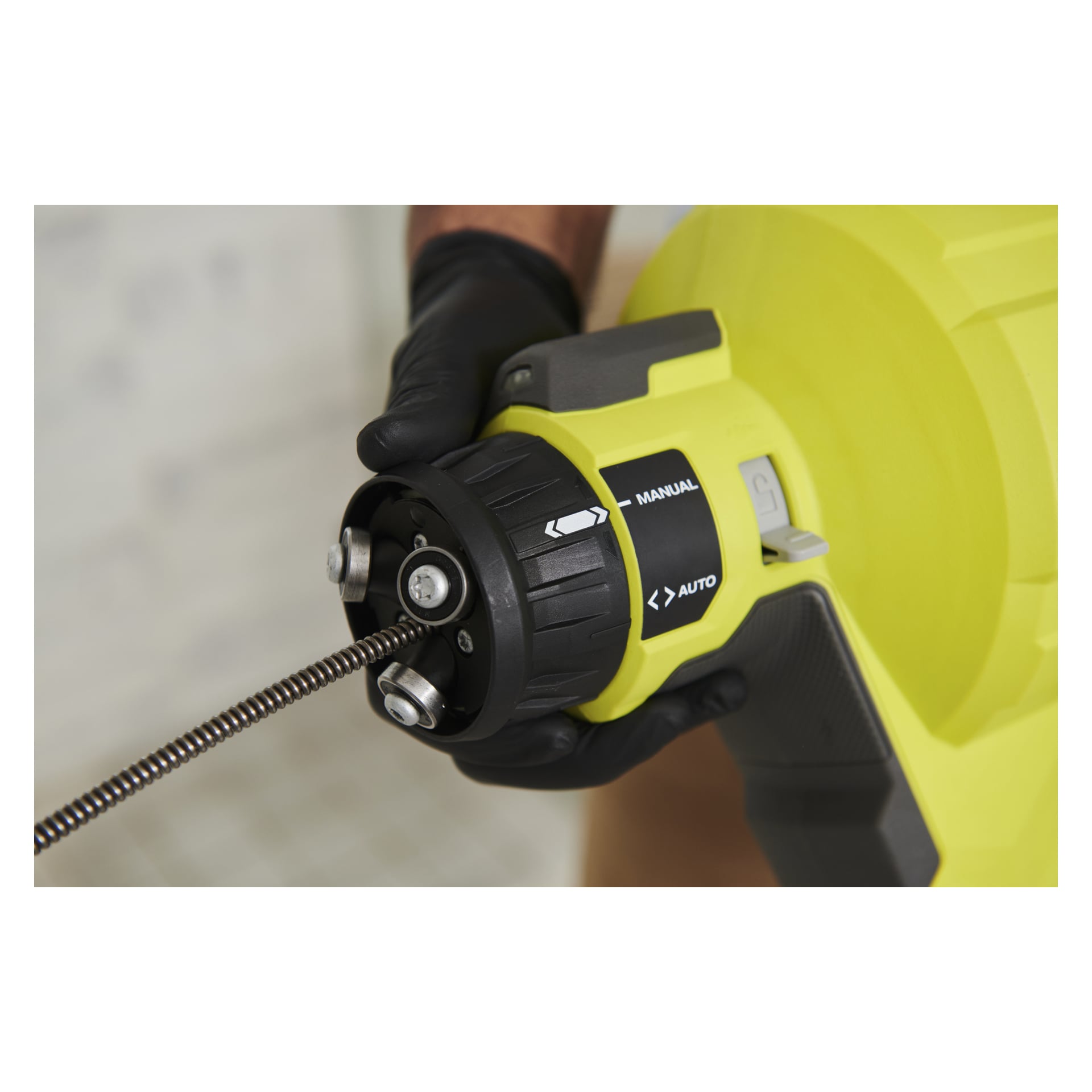 Ręka w rękawiczce używa odpływowego filtra Ryobi One+ RDA18-0, podkreślając pokrętło sterowania oznaczone Manual i Auto, z wysuniętą metalową cewką.