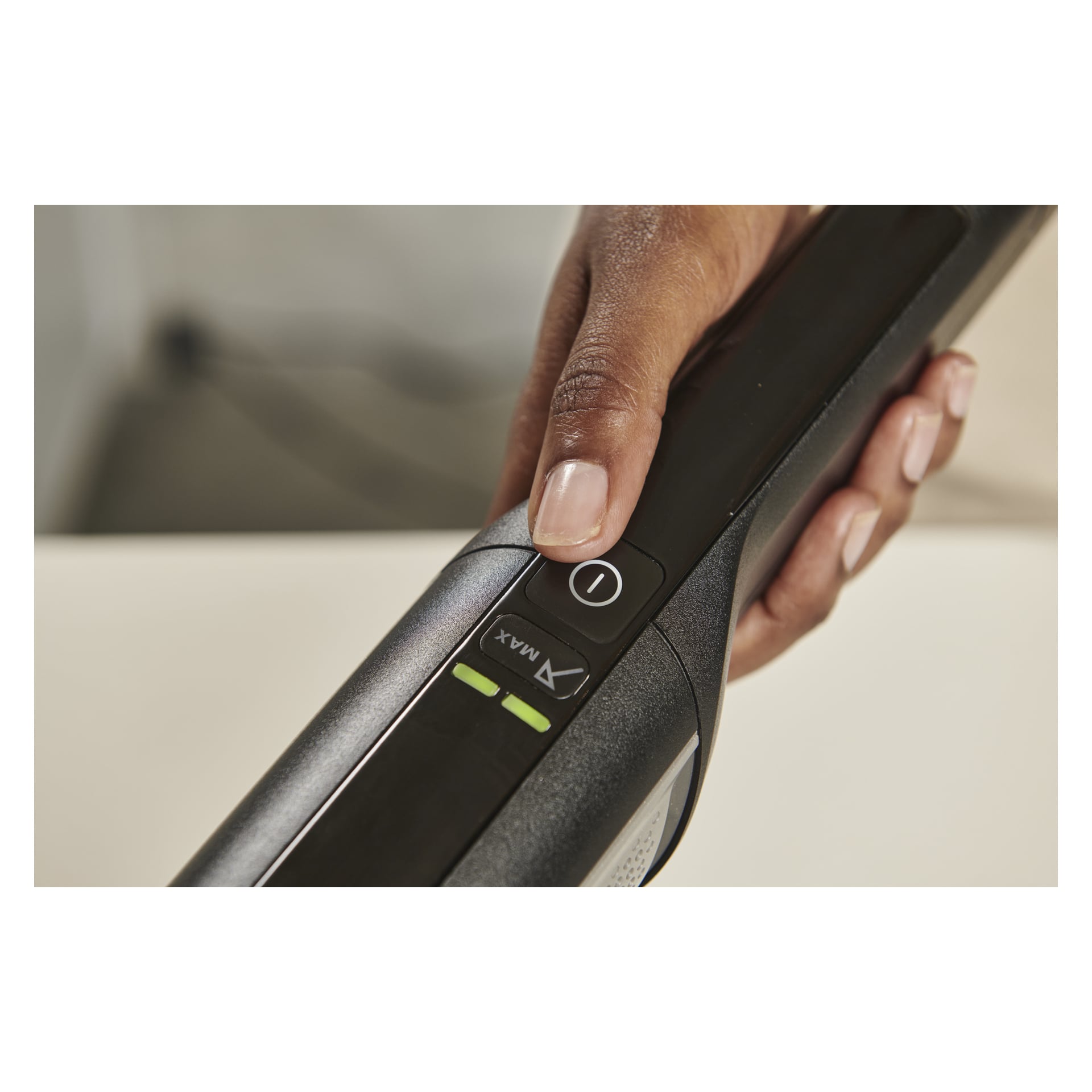 En hand håller i en Ryobi USB Lithium Handhållen dammsugare RHV44-220G, tummen på strömknappen nära MAX- och MIN-indikatorlamporna.