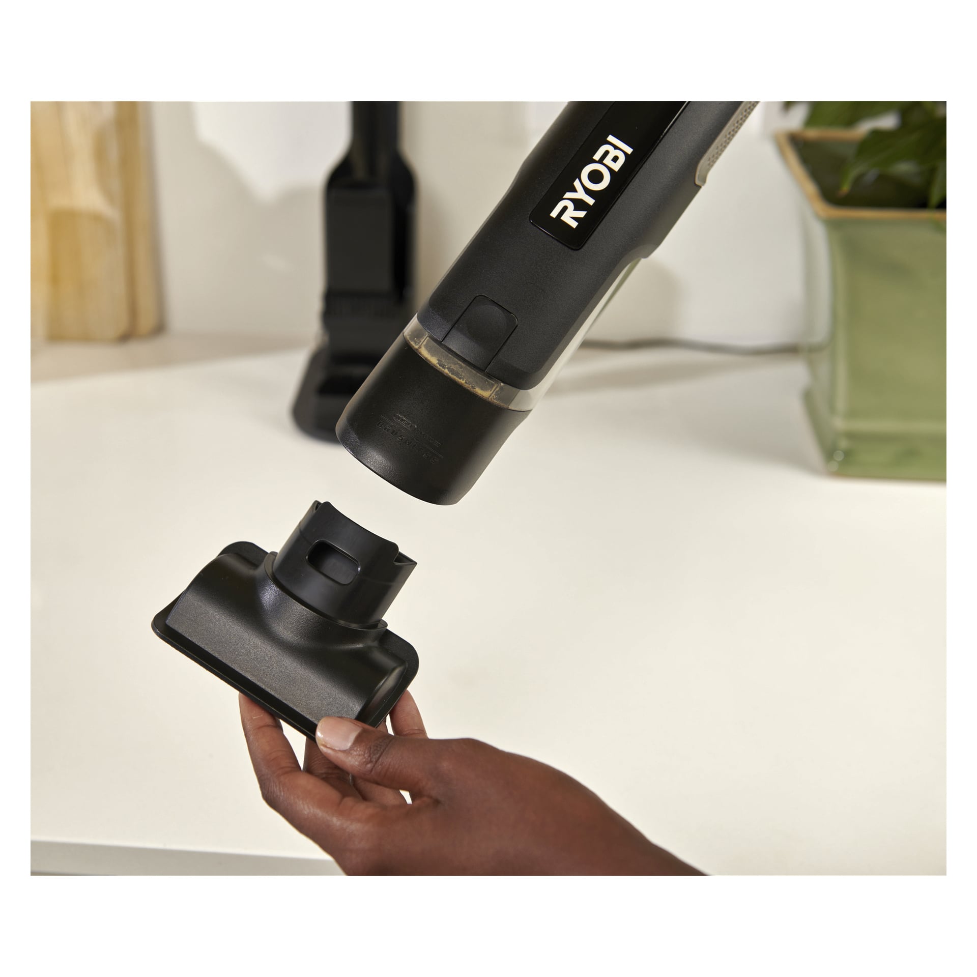 En persons hand placerar en dammsugarkoppling för att koppla den till munstycket på en Ryobi USB Lithium Handhållen dammsugare RHV44-220G.