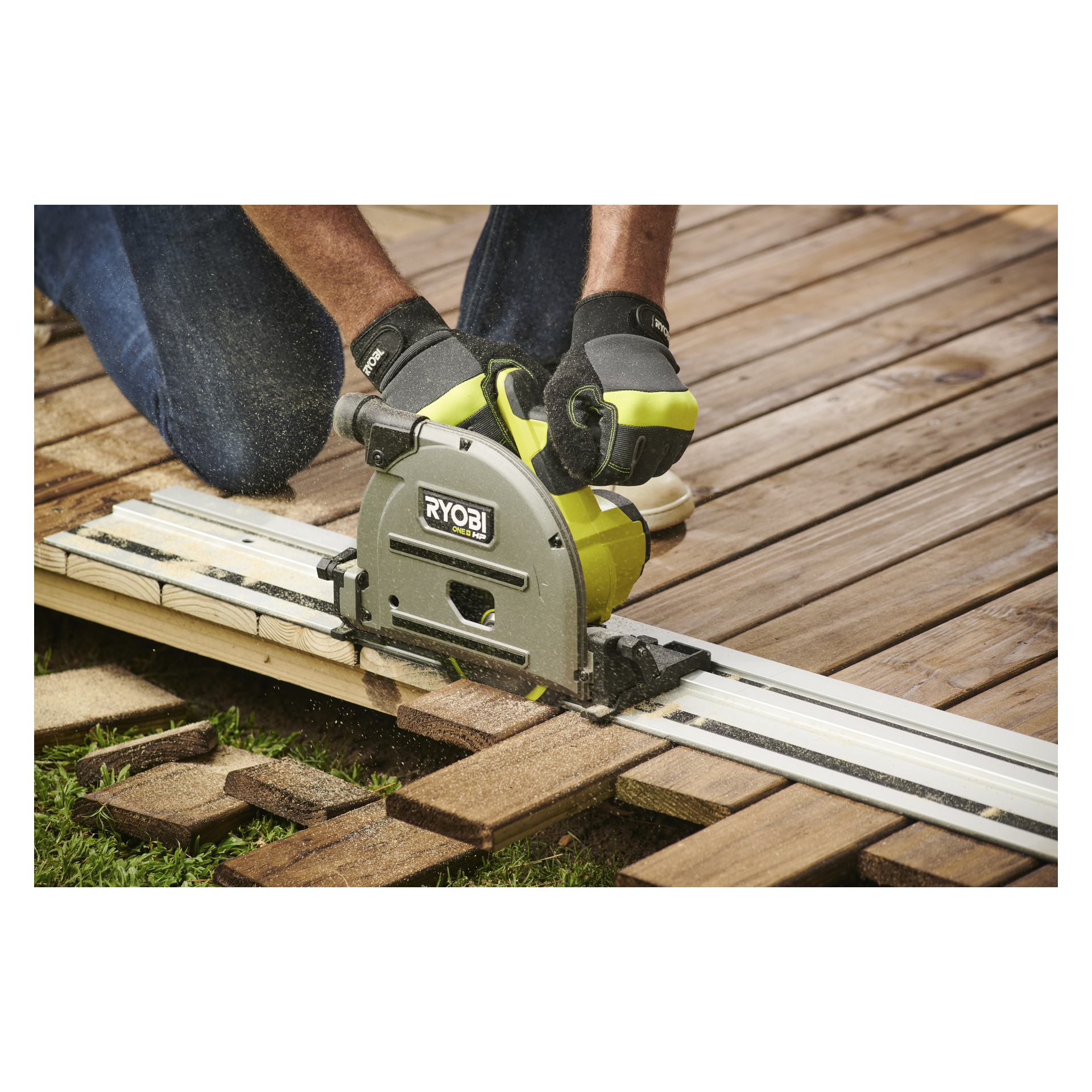 En person med handske använder en Ryobi One+ HP cirkelsåg med styrskena för att såga träplankor på en trall, vilket producerar sågspån.