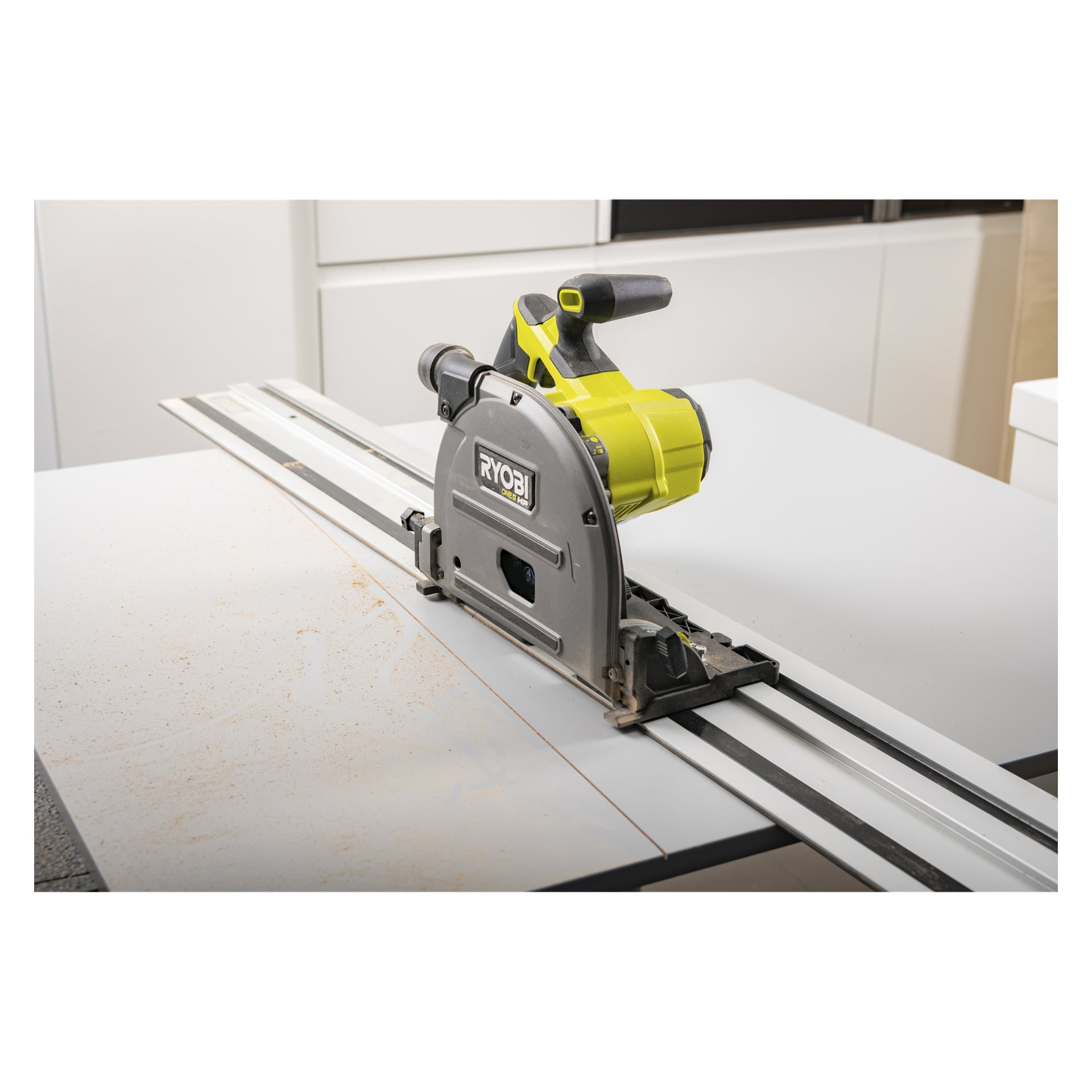 En Ryobi One+ HP-såg på en styrskena R1400GR att göra ett rakt snitt i träet, sågspån utspritt längs skärbanan.