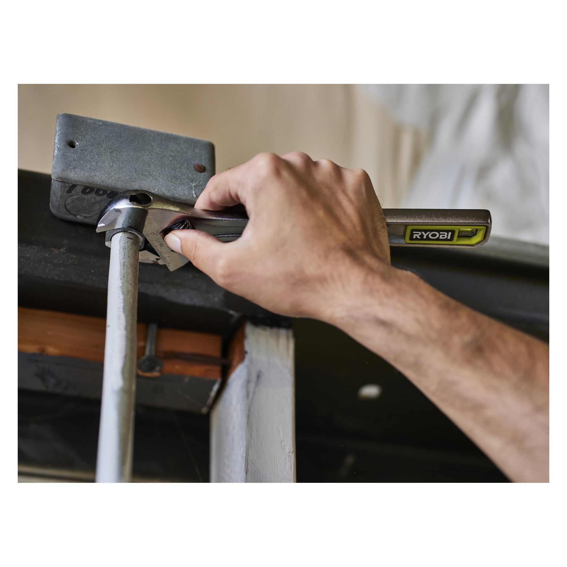 Någon drar åt en bult på ett metallrör som är kopplat till ett fäste med en Ryobi justerbar skiftnyckel RHAW200, troligen för en garageport.