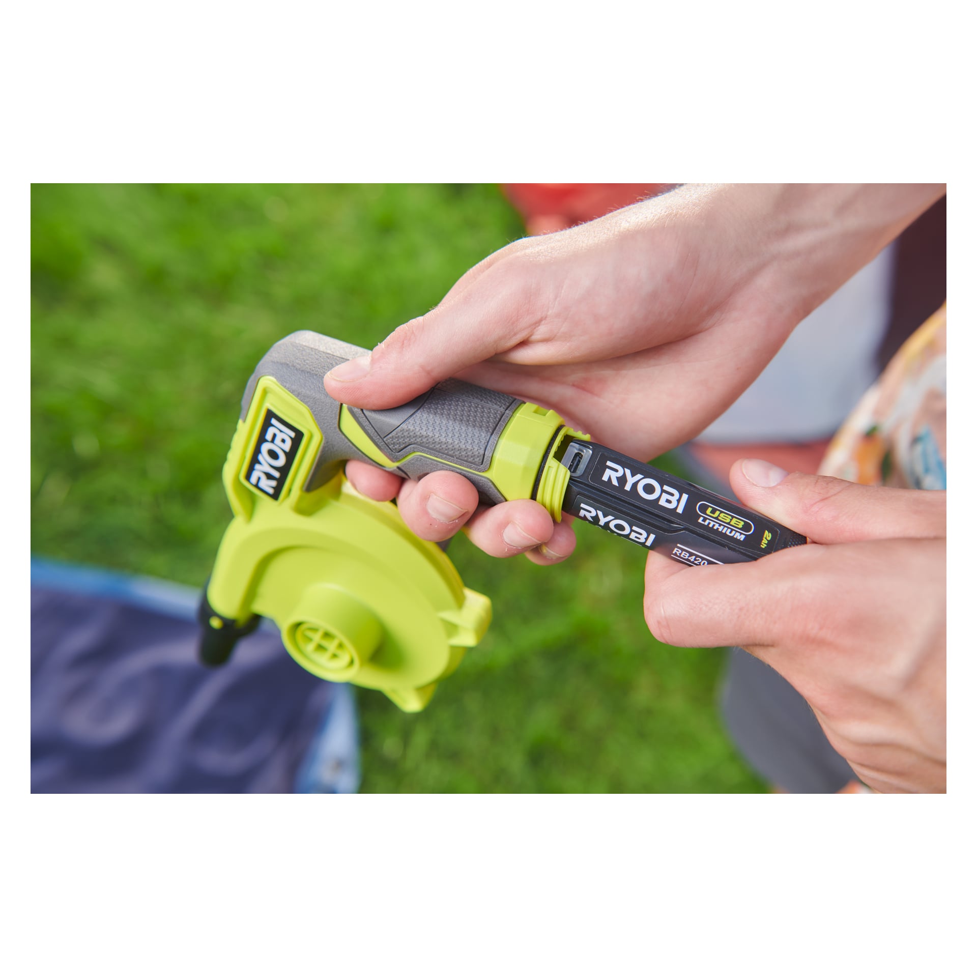 Ktoś umieścił baterię litową USB Ryobi do zielonej pompy powietrza RVI4-0 Ryobi na trawiastej ziemi.