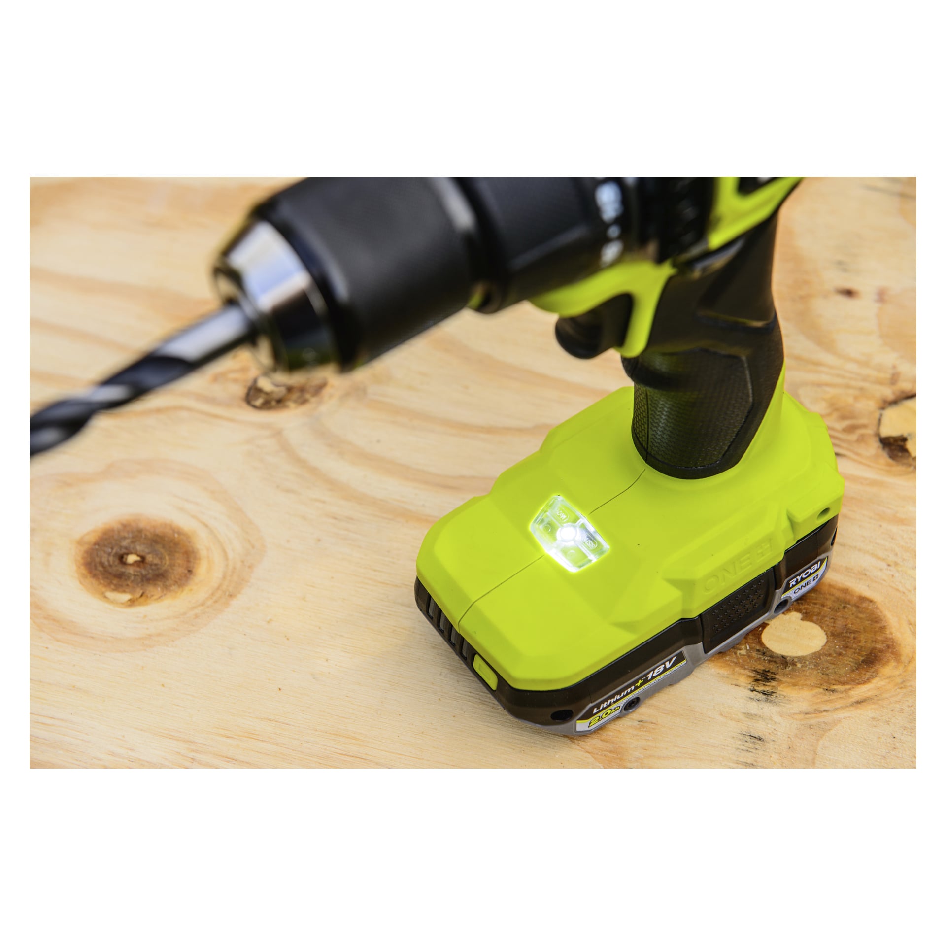Ryobi One+ HP skrutrekker RPD18X1-0 med grønt batteri står på en lys treflate, slått på med batteriets LED-lys som lyser.