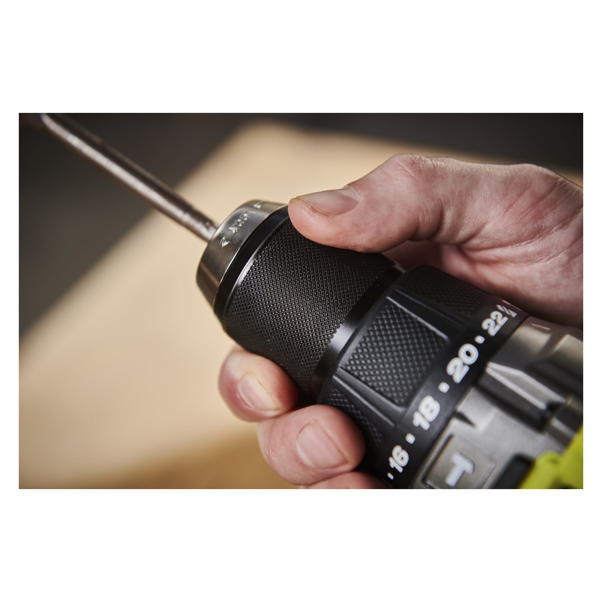En hånd griper Ryobi One+ HP skrutrekkeren RPD18X1-0, og fremhever chuck- og dreiemomentkontrollene med en myk, uskarp bakgrunn.
