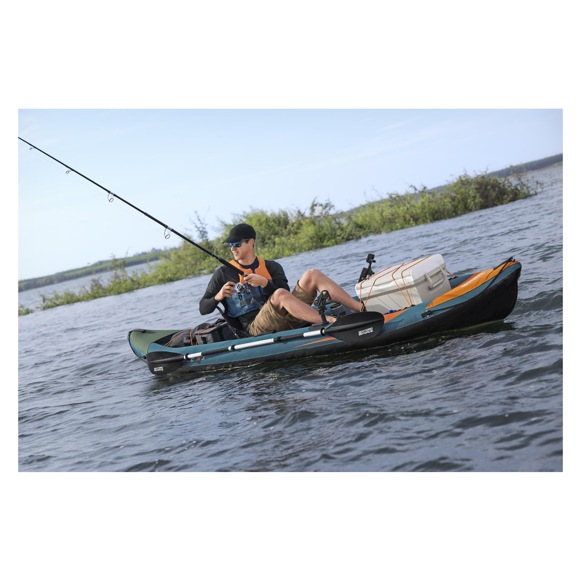 Aurinkolasit ja lakki päässä oleva henkilö kalastaa Bestway Elite X1 -kajakista, jonka takana on kylmälaukku ja varusteet, vettä ja matalia kasveja.