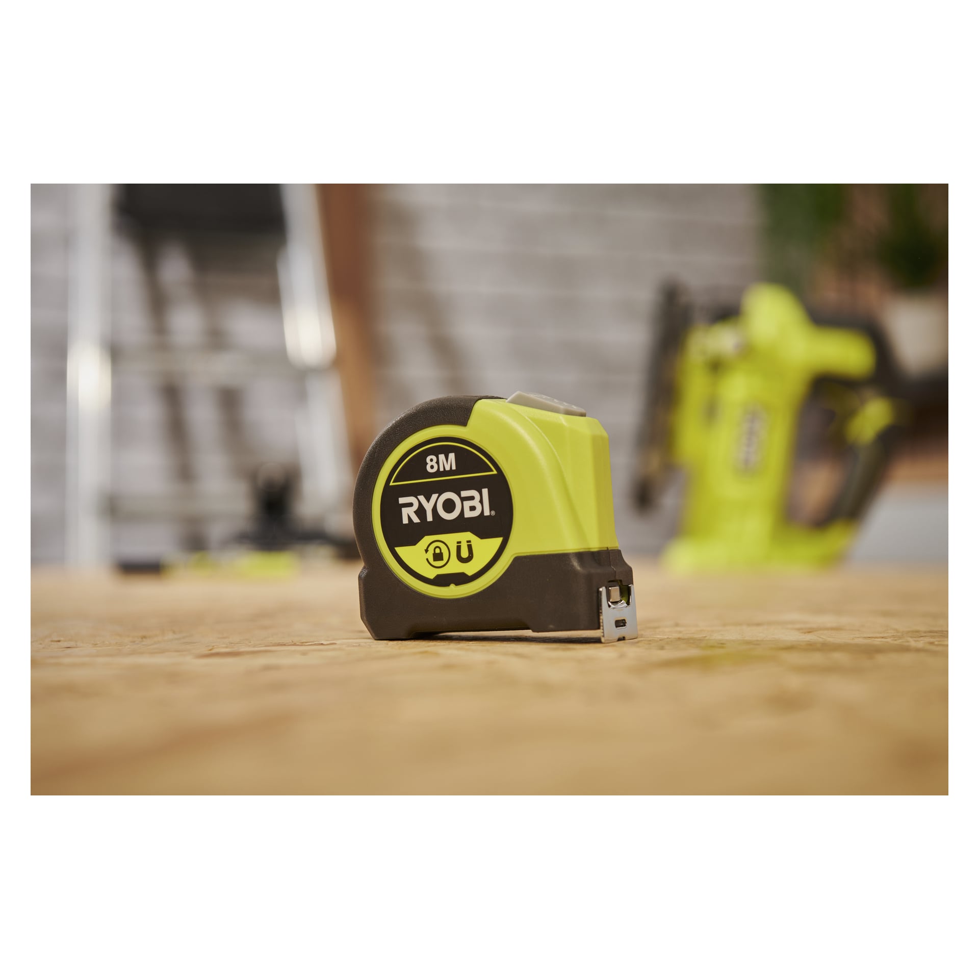 Ett Ryobi RHMTM8-måttband står på trä, med ett grönt elverktyg mjukt ur fokus i bakgrunden.