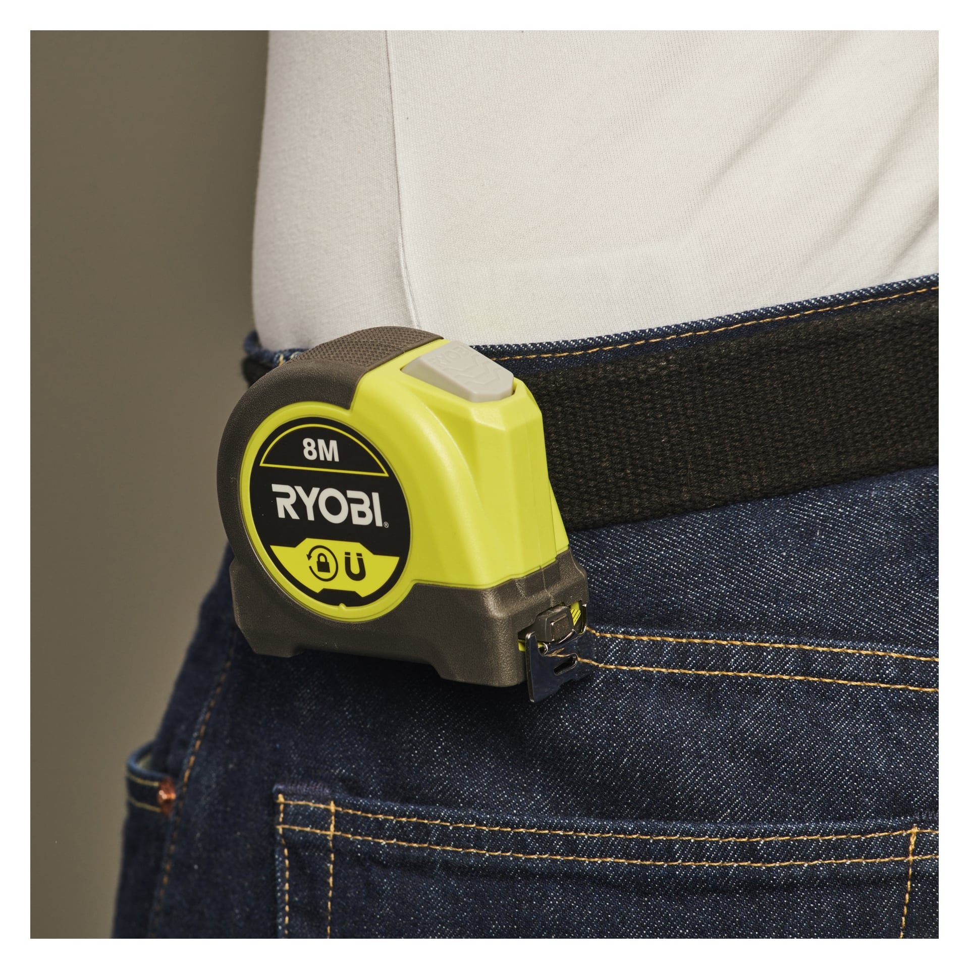 En person i jeans och vit skjorta har ett Ryobi RHMTM8-måttband fäst vid sitt svarta bälte.
