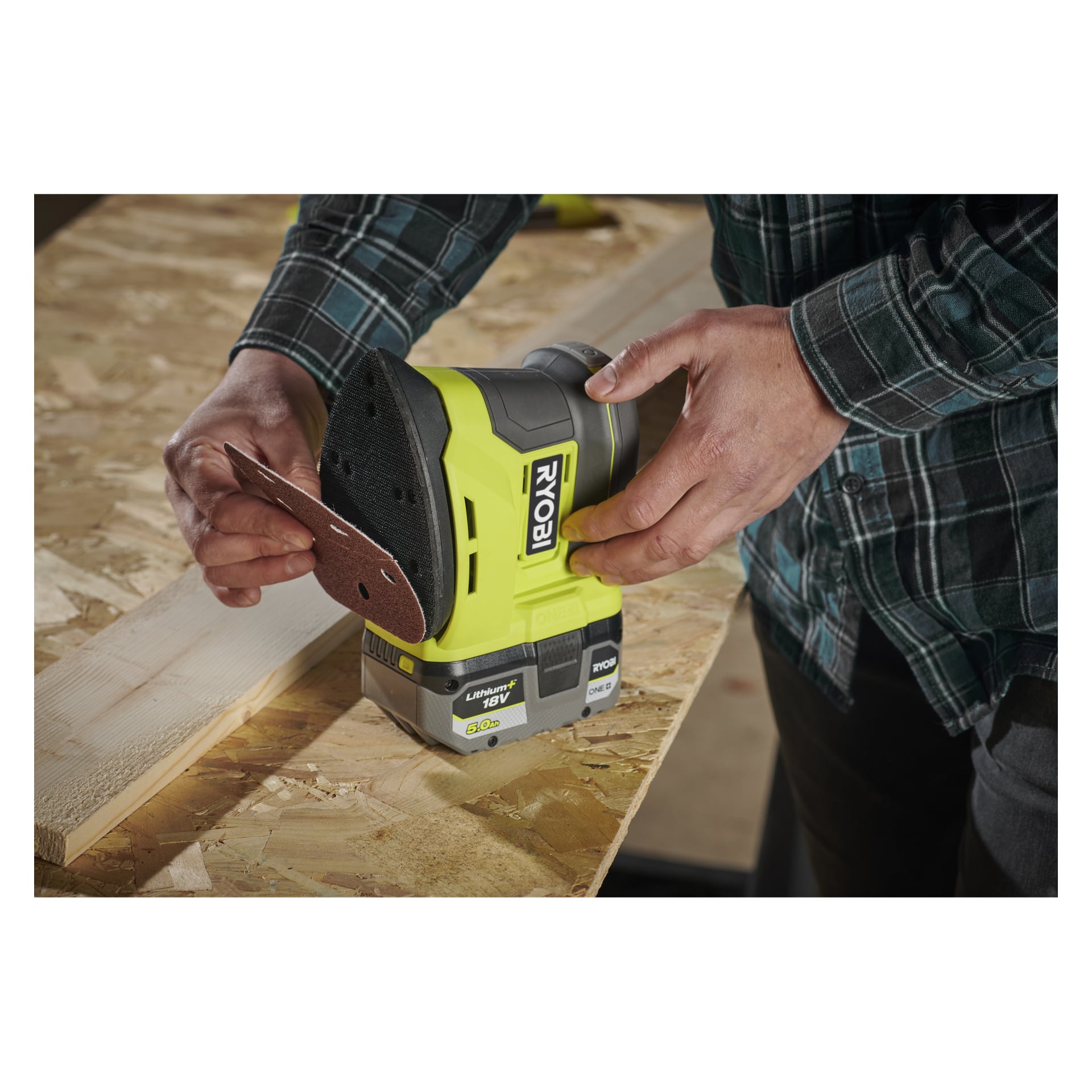 En person som bär en rutig skjorta fäster en triangulär sandpappersplatta på en gul och svart Ryobi One+ Multi-slipare R18PSN-0.