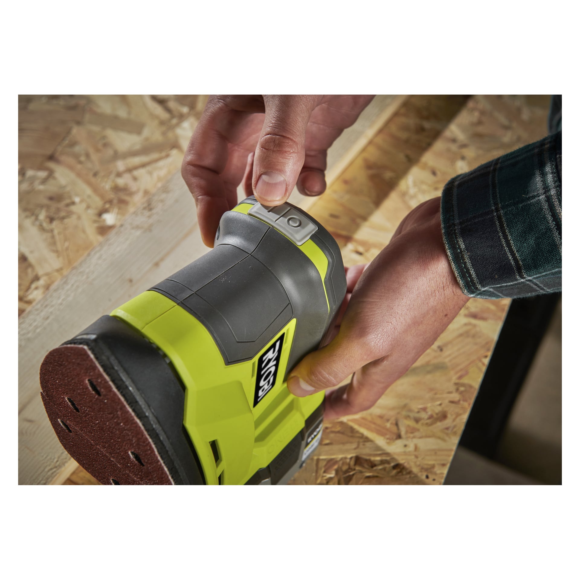 Händerna använder en klargrön och grå Ryobi One+ Multi-slipare R18PSN-0 med slipplatta på en träyta.