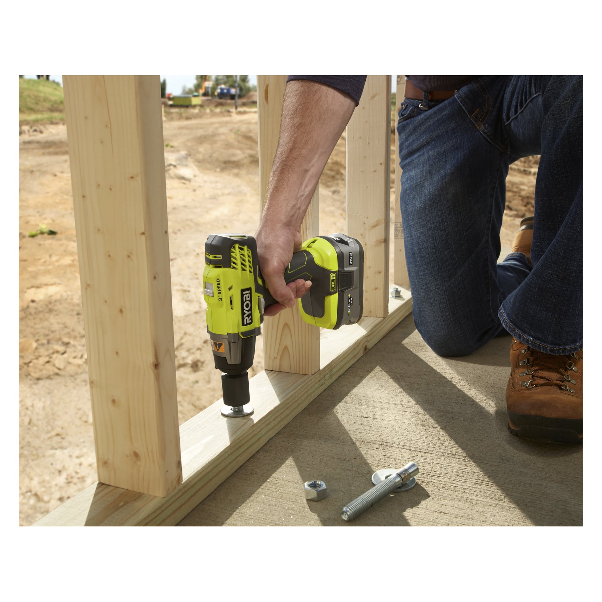 Någon knäböjer på betong på en byggarbetsplats och använder en Ryobi One+ Battery slagnyckel för att fästa en bult i en träram.