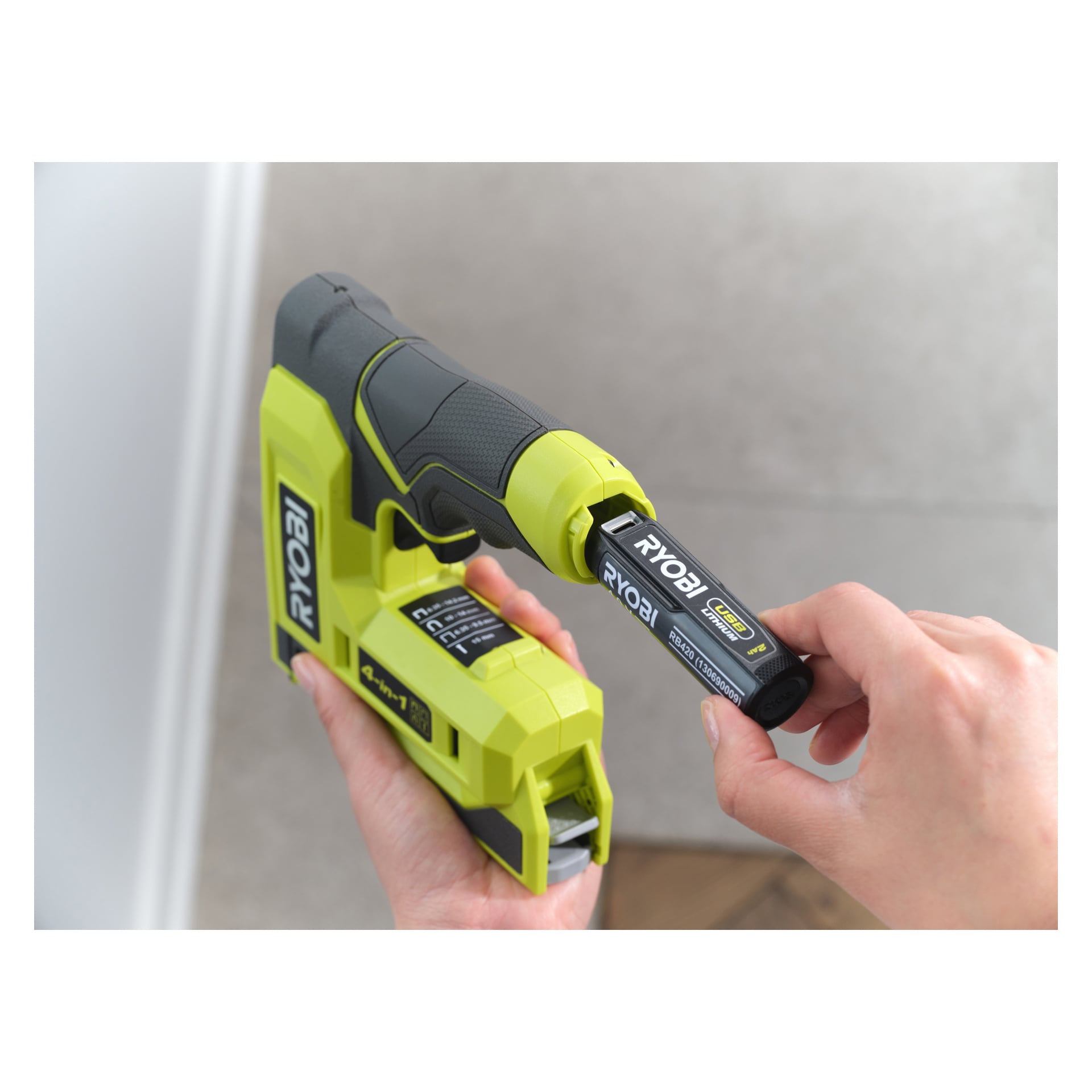 Noen setter et Ryobi USB Lithium 4V-batteri i en grønn og svart RST4-0 stiftepistol, og holder hver gjenstand i separate hender.
