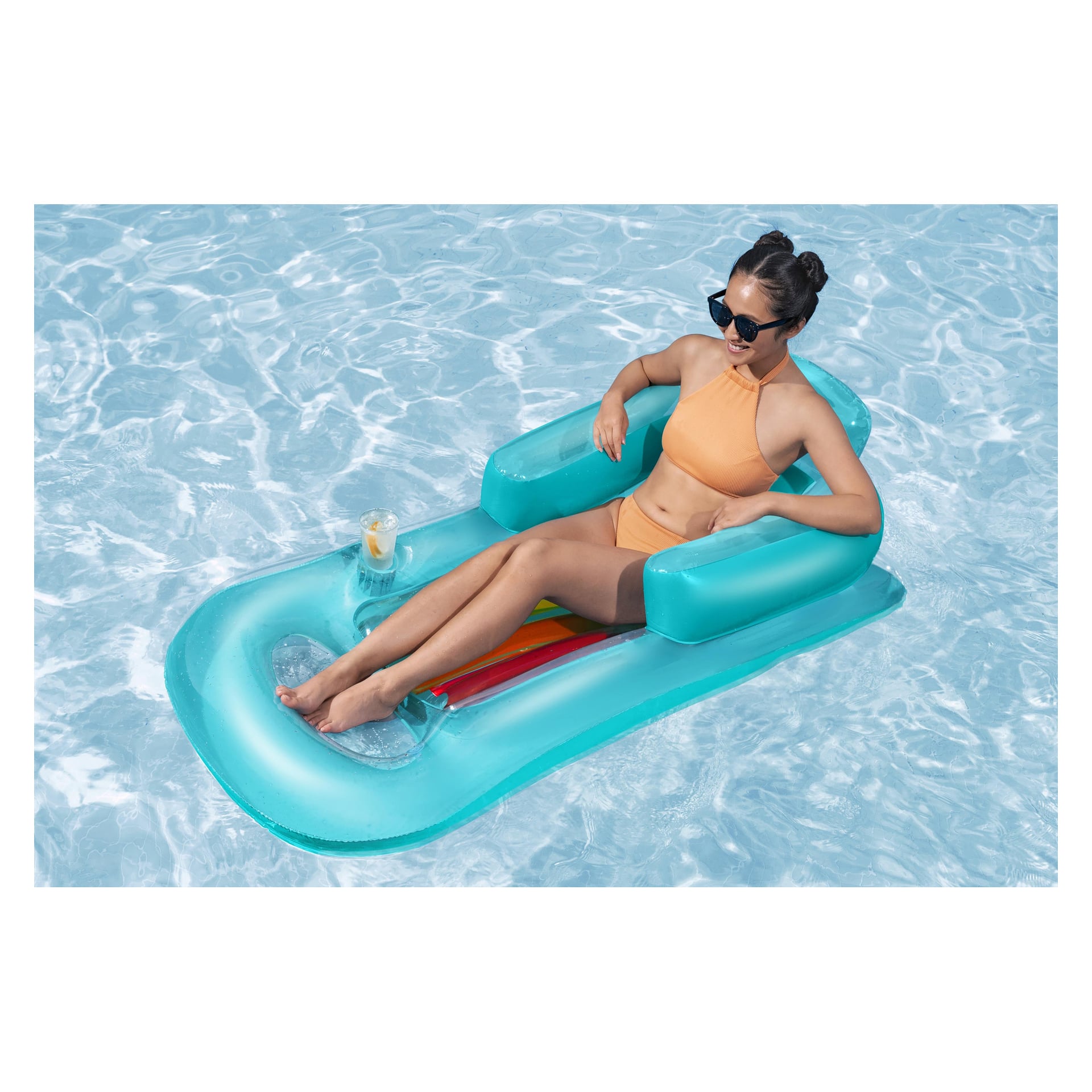En kvinna i orange bikini och solglasögon ligger på en flytande Bestway Sun-madrass, dricker i mugghållare, i klart vatten.