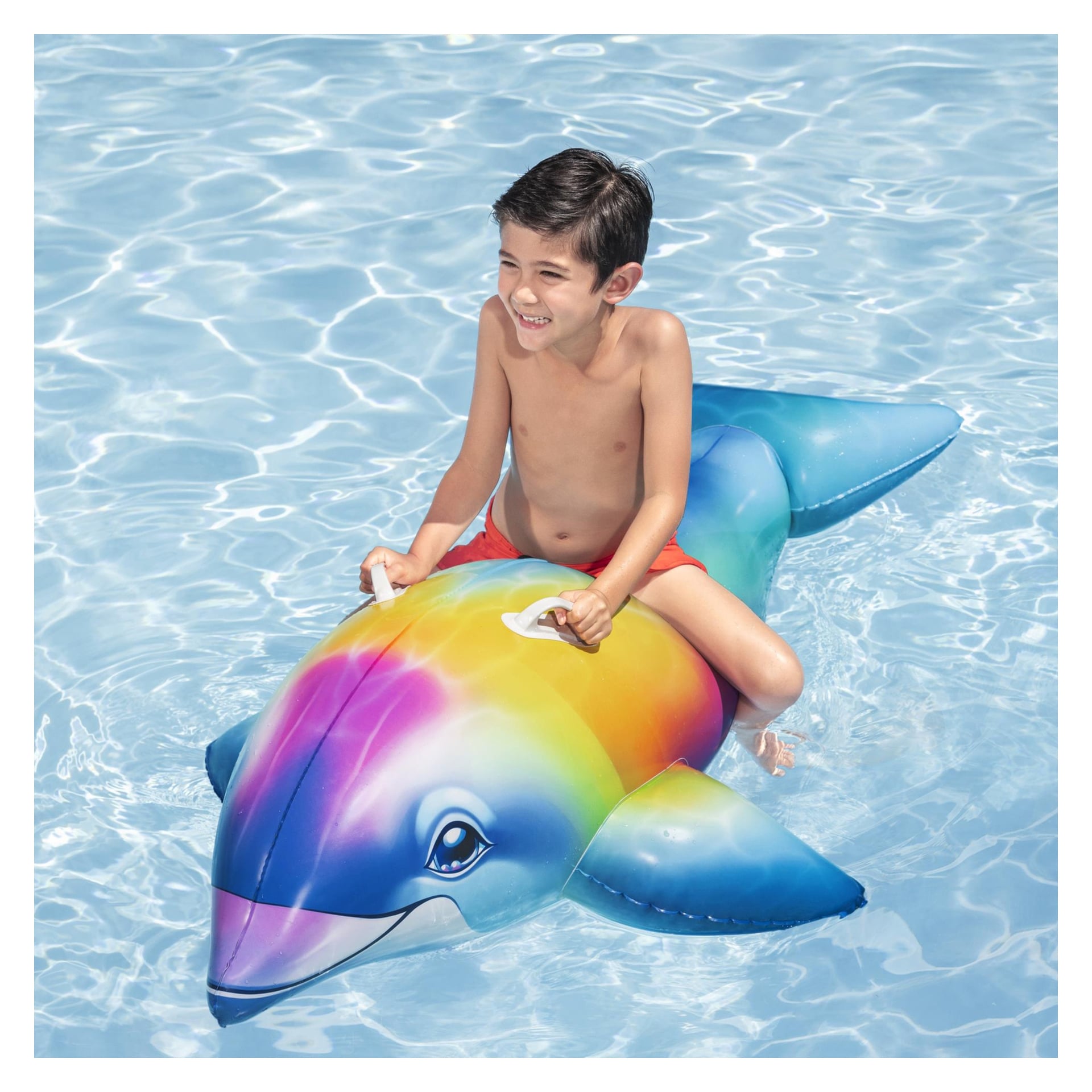 Wesoły chłopiec w czerwonych kąpielówkach siedzi na żywym, nadmuchiwanym, chwytającym białym uchwytie Bestway Dolphin Daydream Ride-On w basenie.