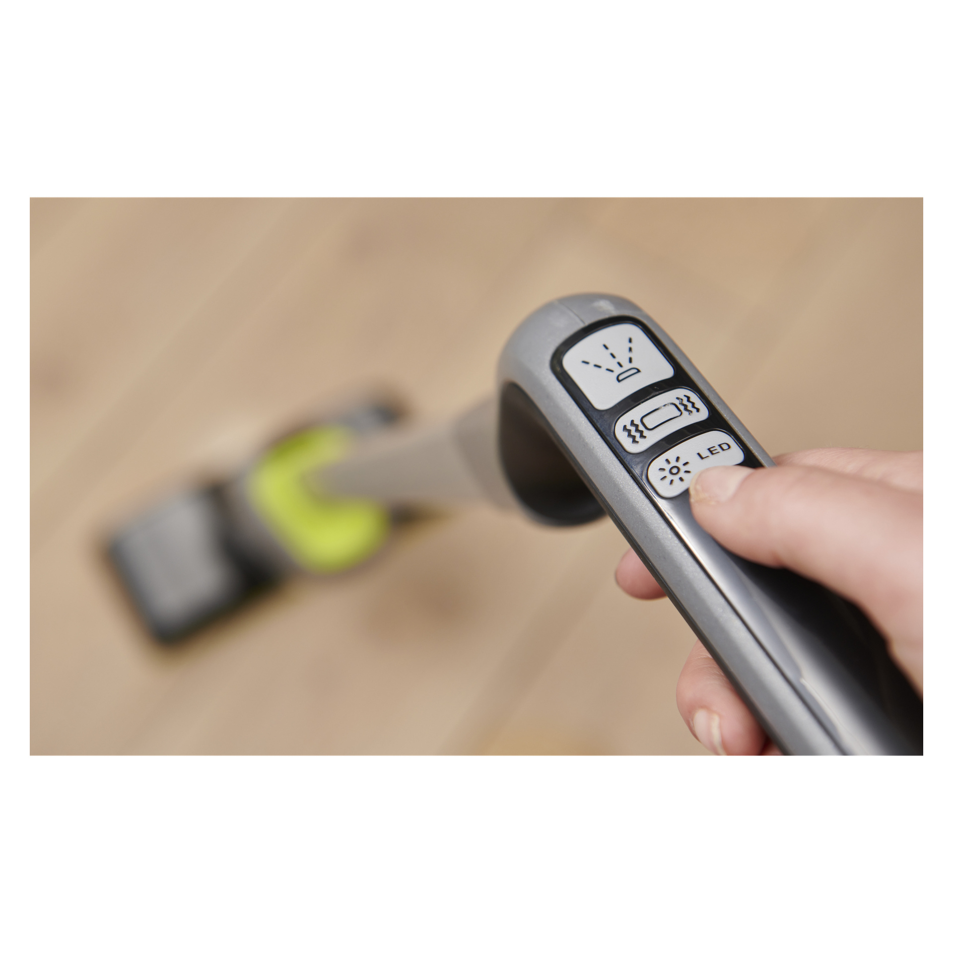 En hand väljer en av tre märkta knappar (ljus, borste, LED) på en Ryobi-spraymopp, vars mopphuvud vilar på ett trägolv.