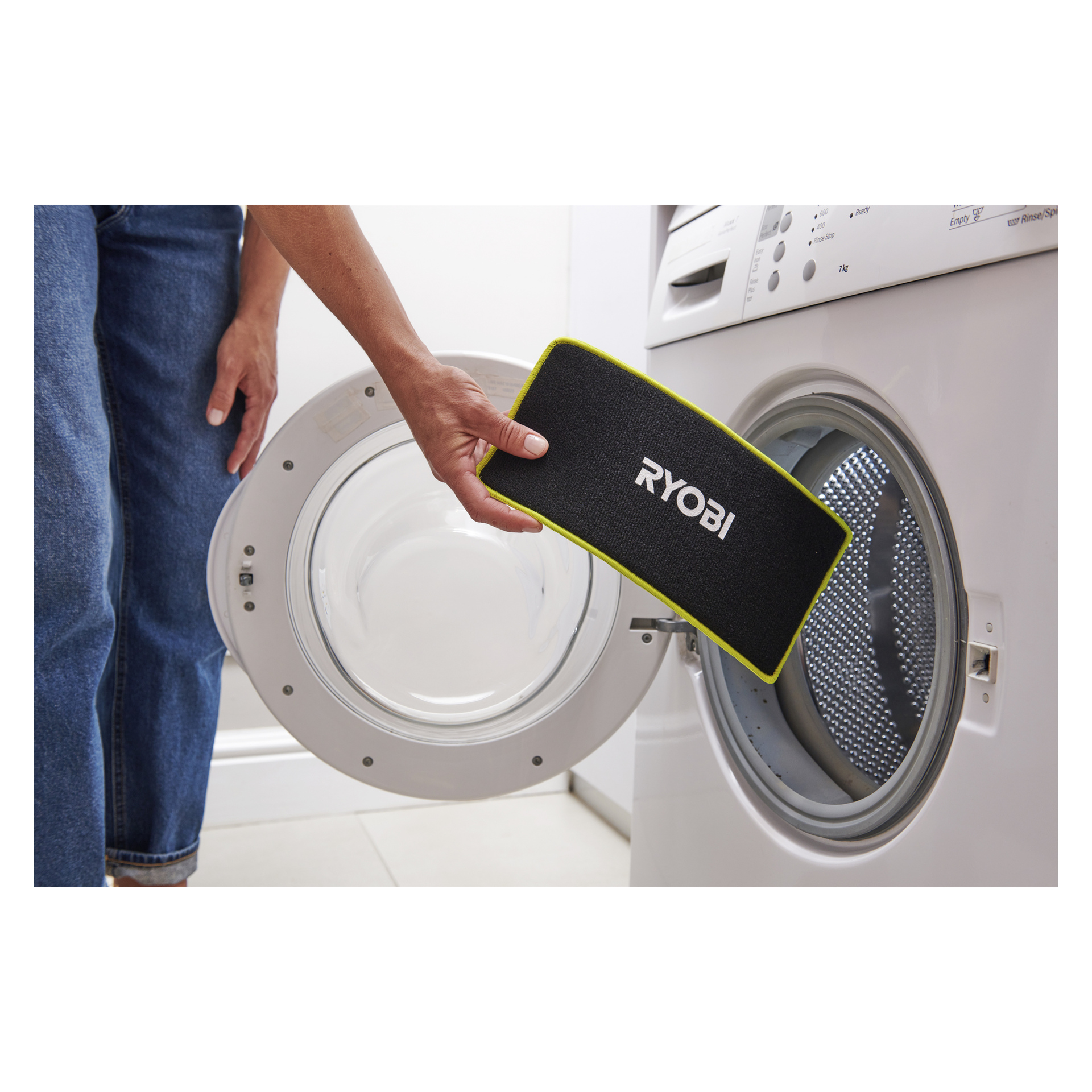Någon sätter in en svart Ryobi USB Lithium Battery spraymopp RSM4-120G med gul kant i en öppen frontmatad tvättmaskin.