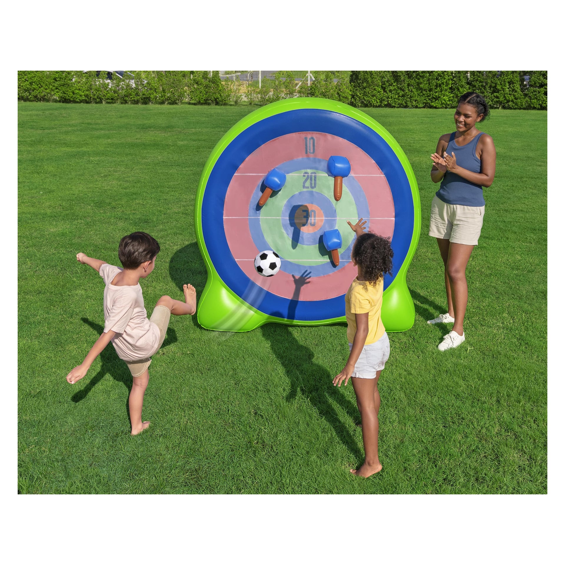 En pojke sparkar en fotboll mot Bestway Inflatable Dartavla Backyard Bullseye 2-i-1-spelet medan en flicka och en kvinna ser på.