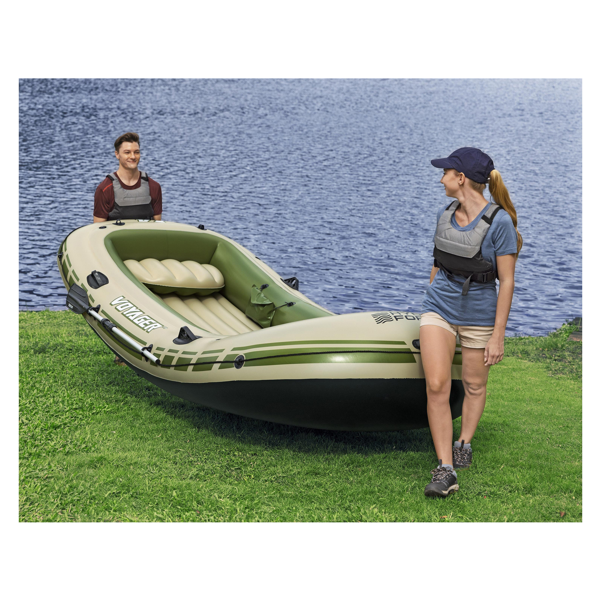 To personer i redningsvester står på gresset ved innsjøen, holder en grønn og beige Voyager X4 oppblåsbar flåte, klar til å skyte ut.