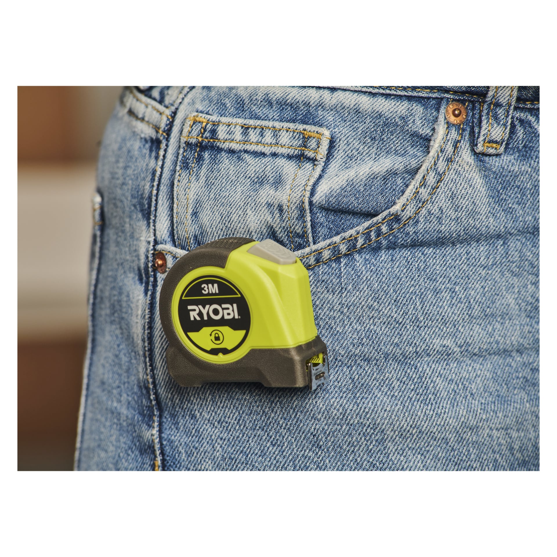 Ett Ryobi RHMT3-måttband är fäst i framfickan på någon som bär blå jeans.