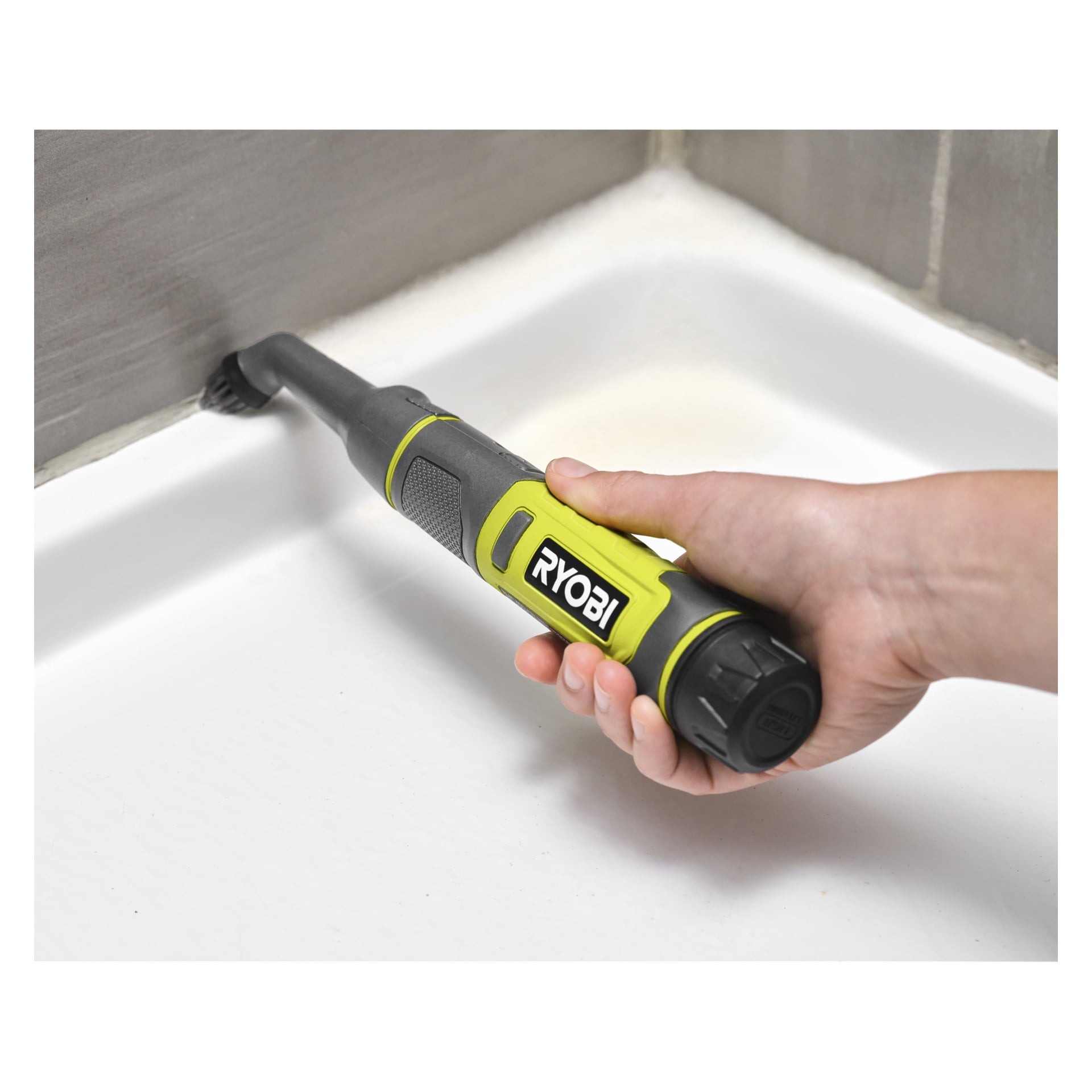 En hand rengör hörnet där badkaret möter den kaklade väggen med hjälp av ett Ryobi USB Lithium Brush-set RDS4A1, vilket visar dess skrubbkraft.