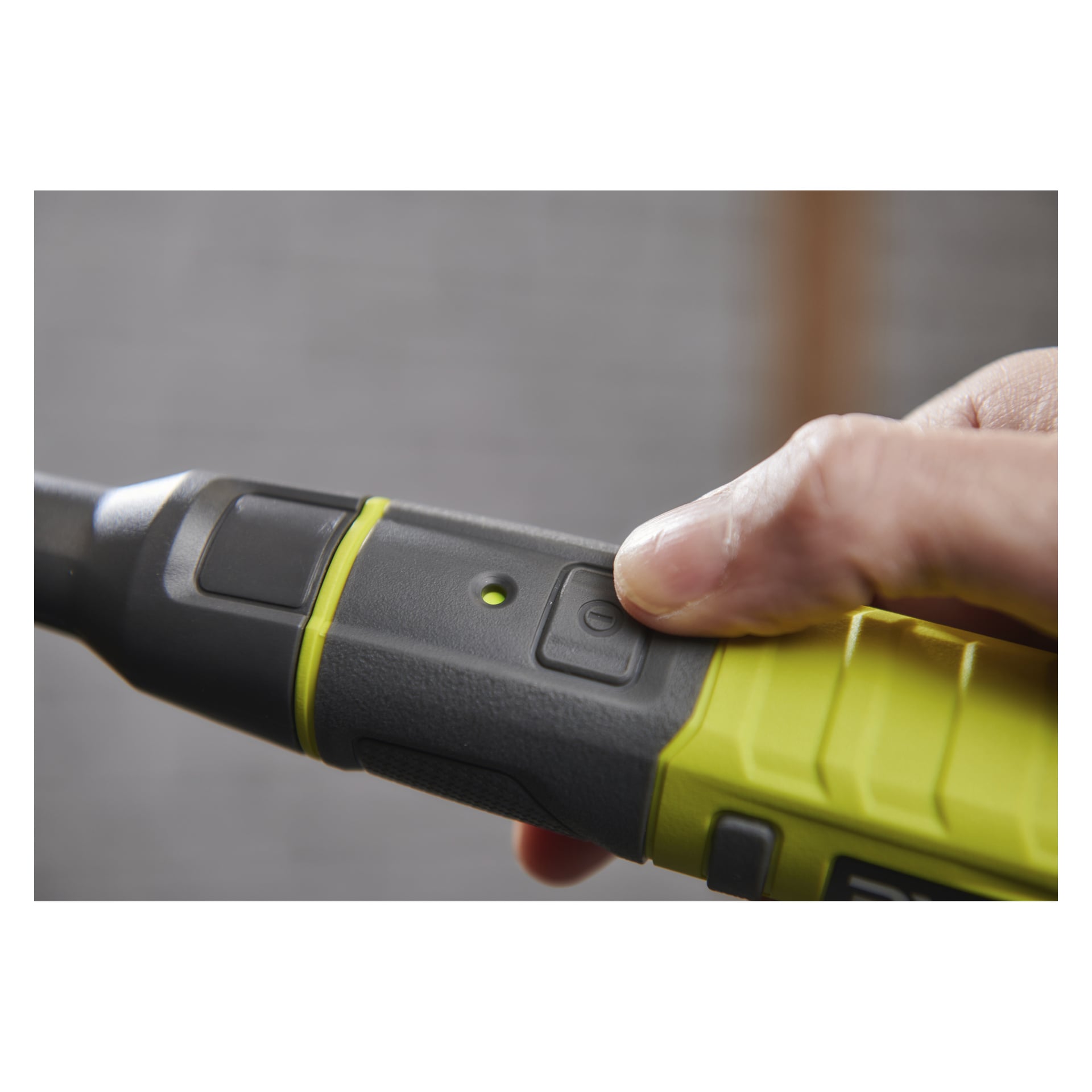 En hand trycker på strömknappen på Ryobi USB Lithium Battery rengöringsborste RDS4-0 medan en grön indikatorlampa lyser i närheten.