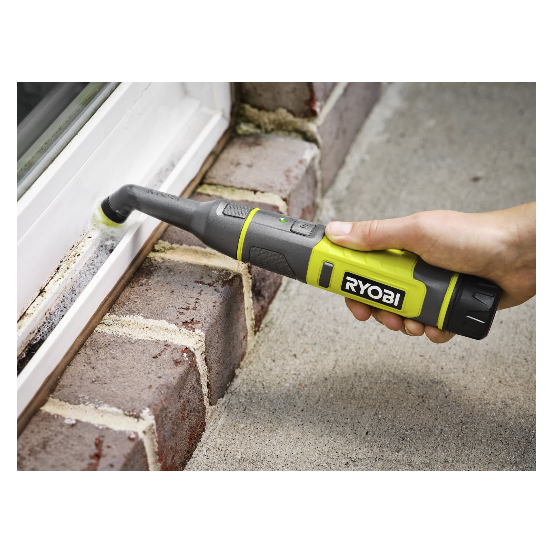 Någon rengör ett fönsterramshörn nära en tegelavsats med en Ryobi USB Lithium detaljborste med en liten rund fäste.