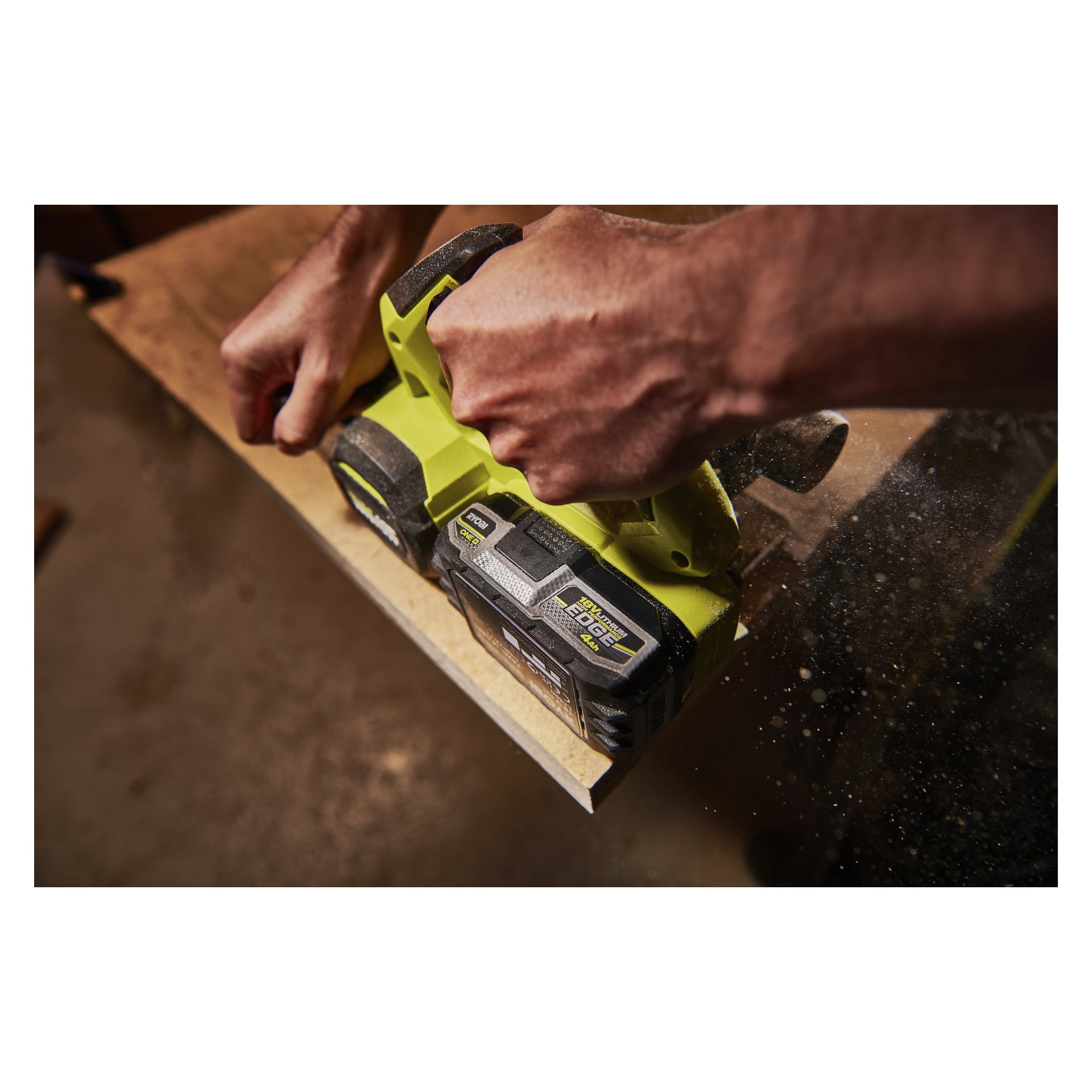 Man använder en Ryobi One+ HP Battery Edge RB1840E sladdlös hyvel på en brädas kant, vilket sprider träspån och damm.