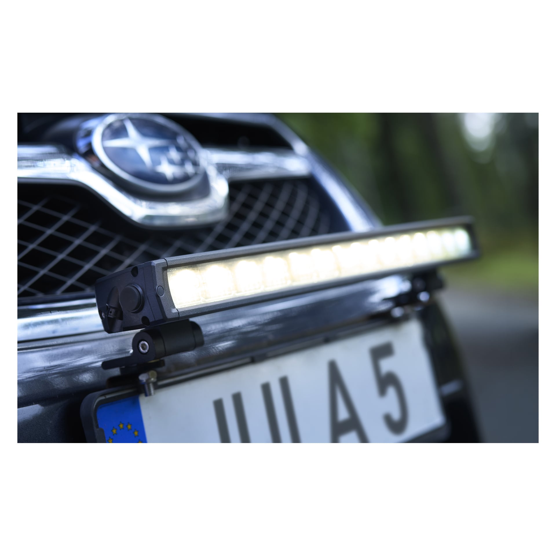Närbild på en bils frontgrill med en LED-ljusramp ovanför en registreringsskylt som visar IIIA5 och en suddig Subaru-logga bakom.